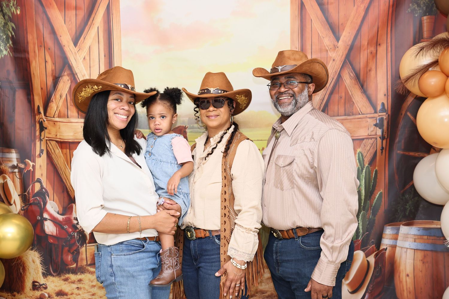 Family of four in cowboy hats posing in front of a rustic barn backdrop at a western-themed event.