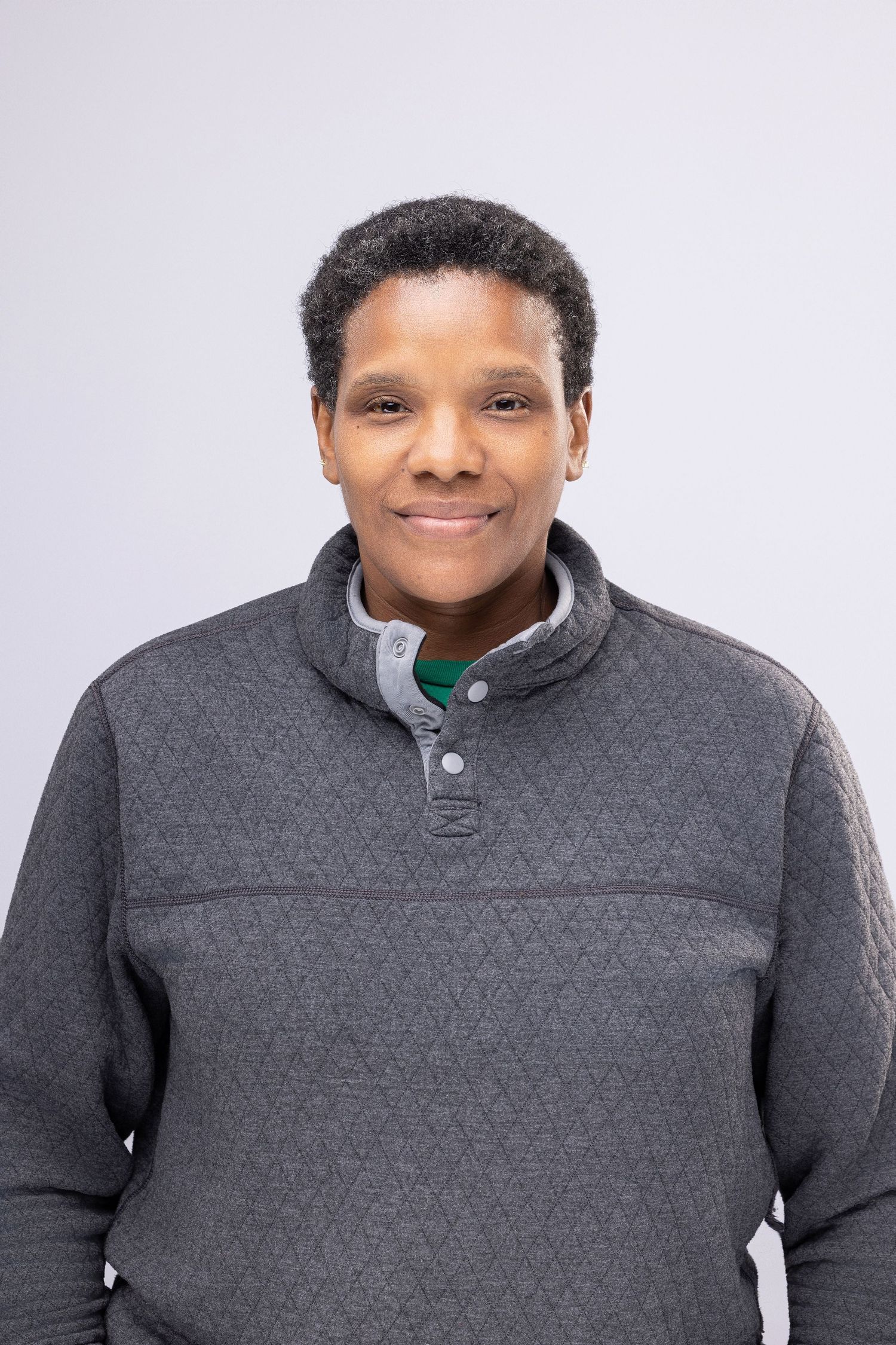 Person in gray quilted sweater posing against white studio backdrop.