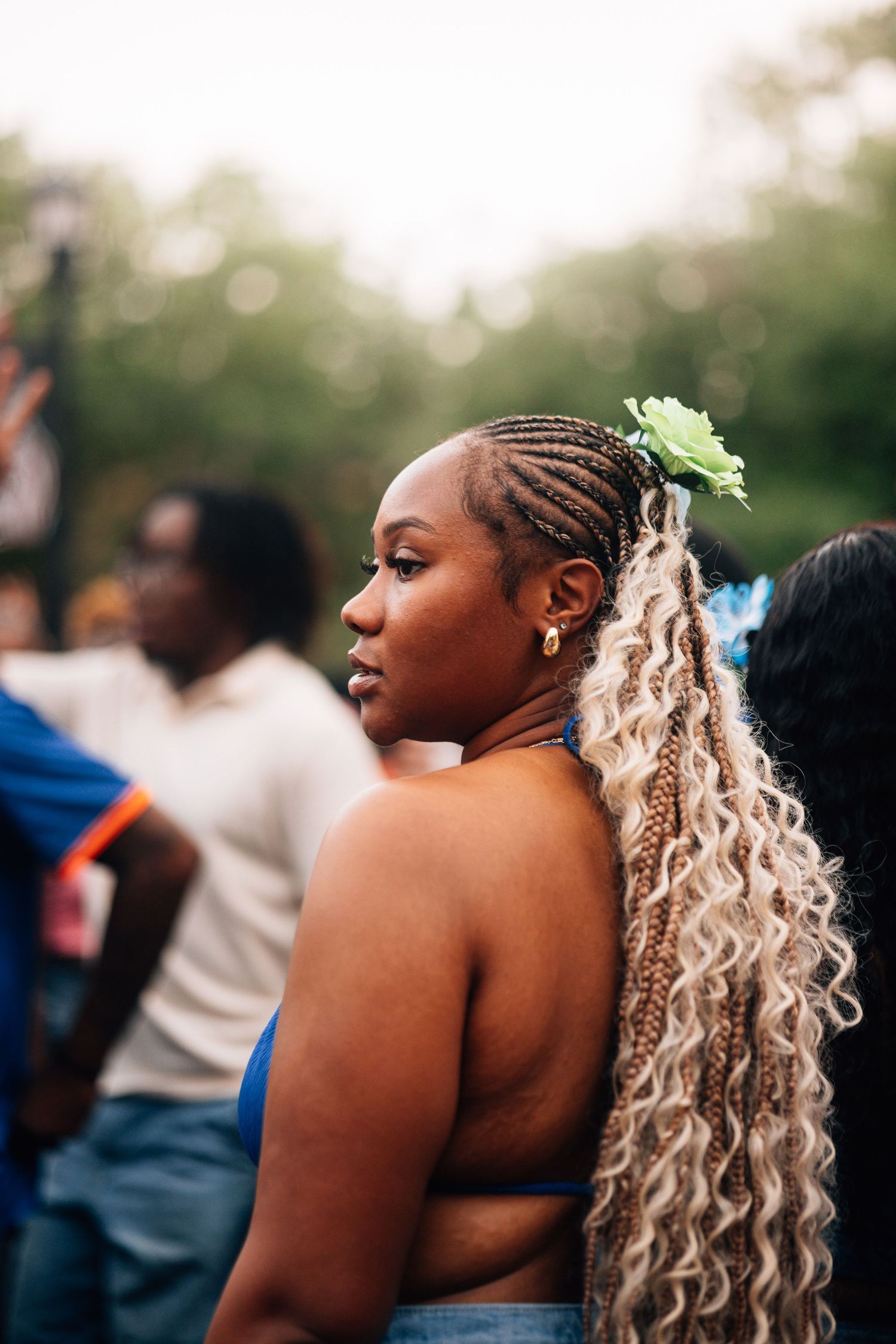 A woman with blonde curly hair extensions styled in a ponytail dances at an outdoor event, photographed from behind.