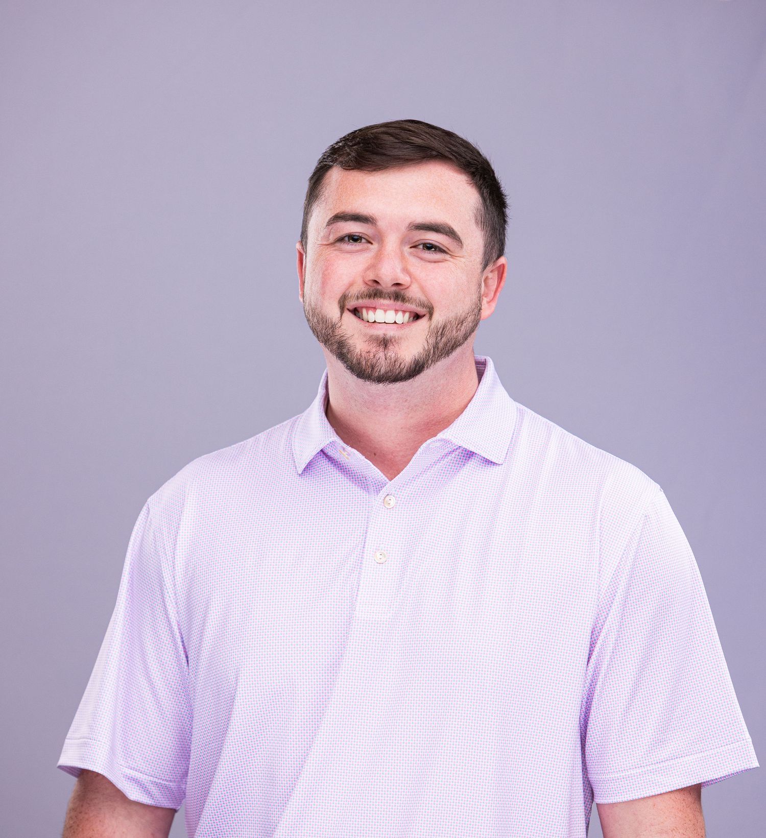 Professional headshot of person in white polo shirt smiling against purple background.