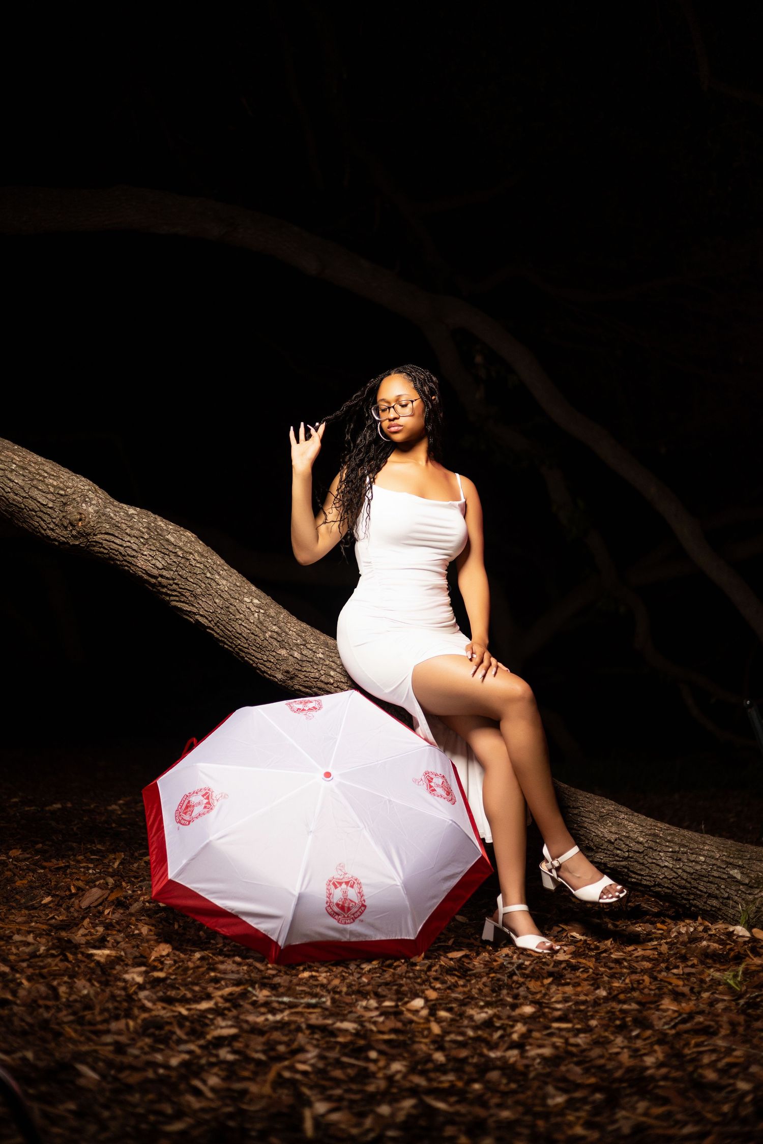 Artistic portrait with a white umbrella and dramatic lighting on a tree branch at night.