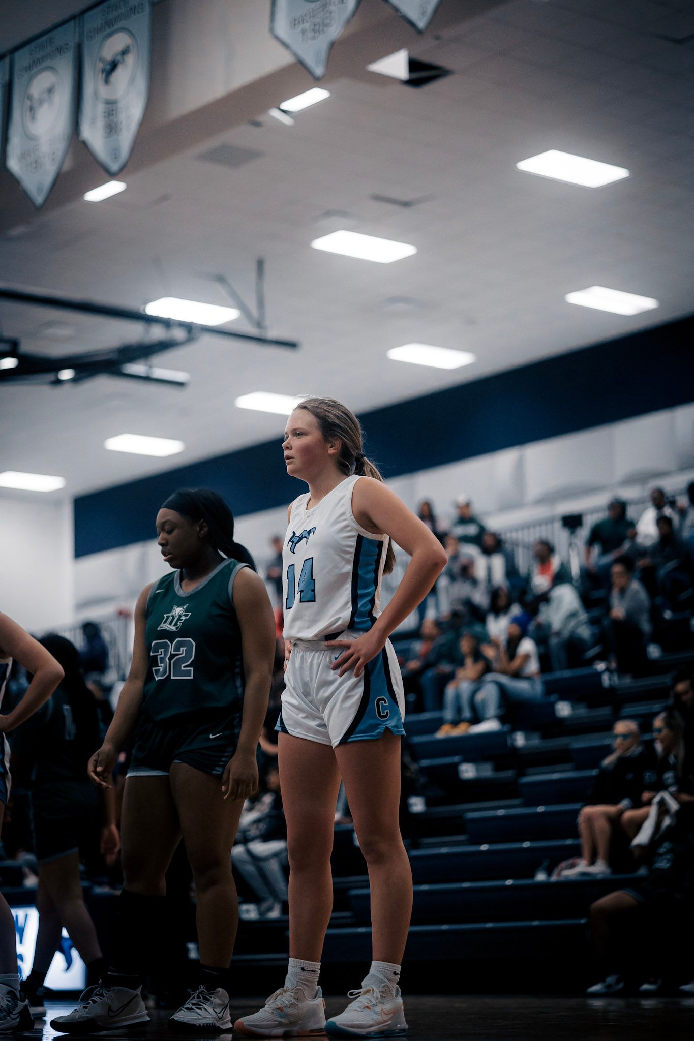 Two basketball players standing on sideline during game in high school gymnasium.