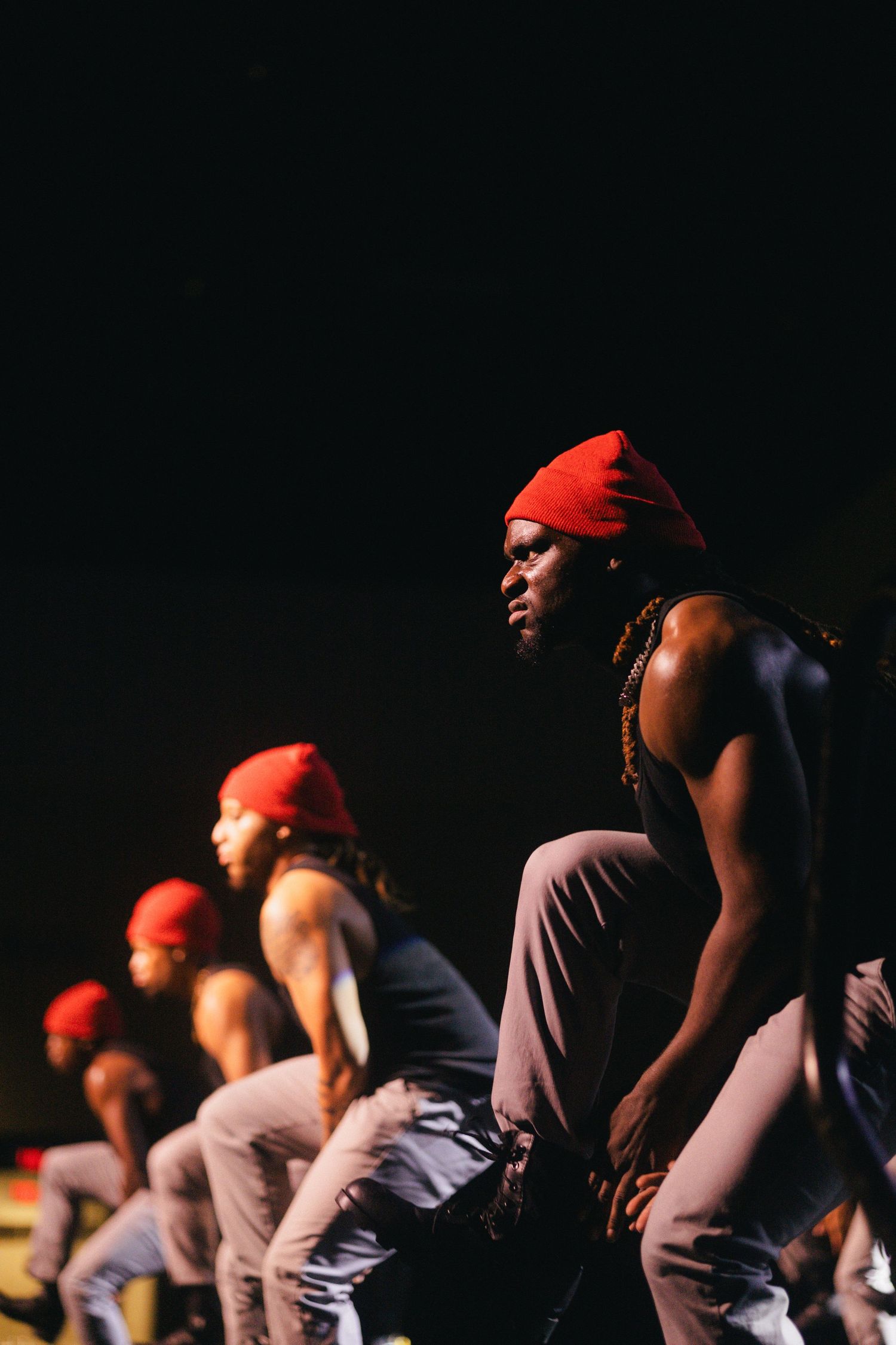 Nupes in red beanies perform a synchronized dance routine against a dark background on stage.