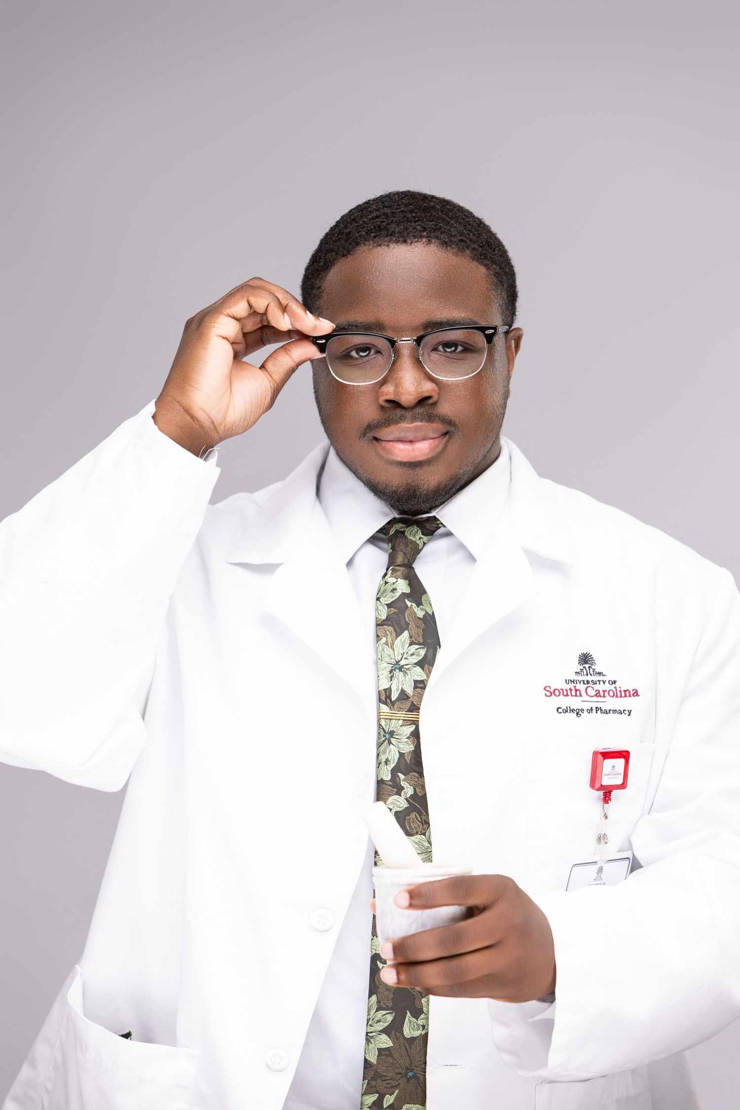 Professional portrait of medical professional in white coat and patterned tie adjusting glasses.