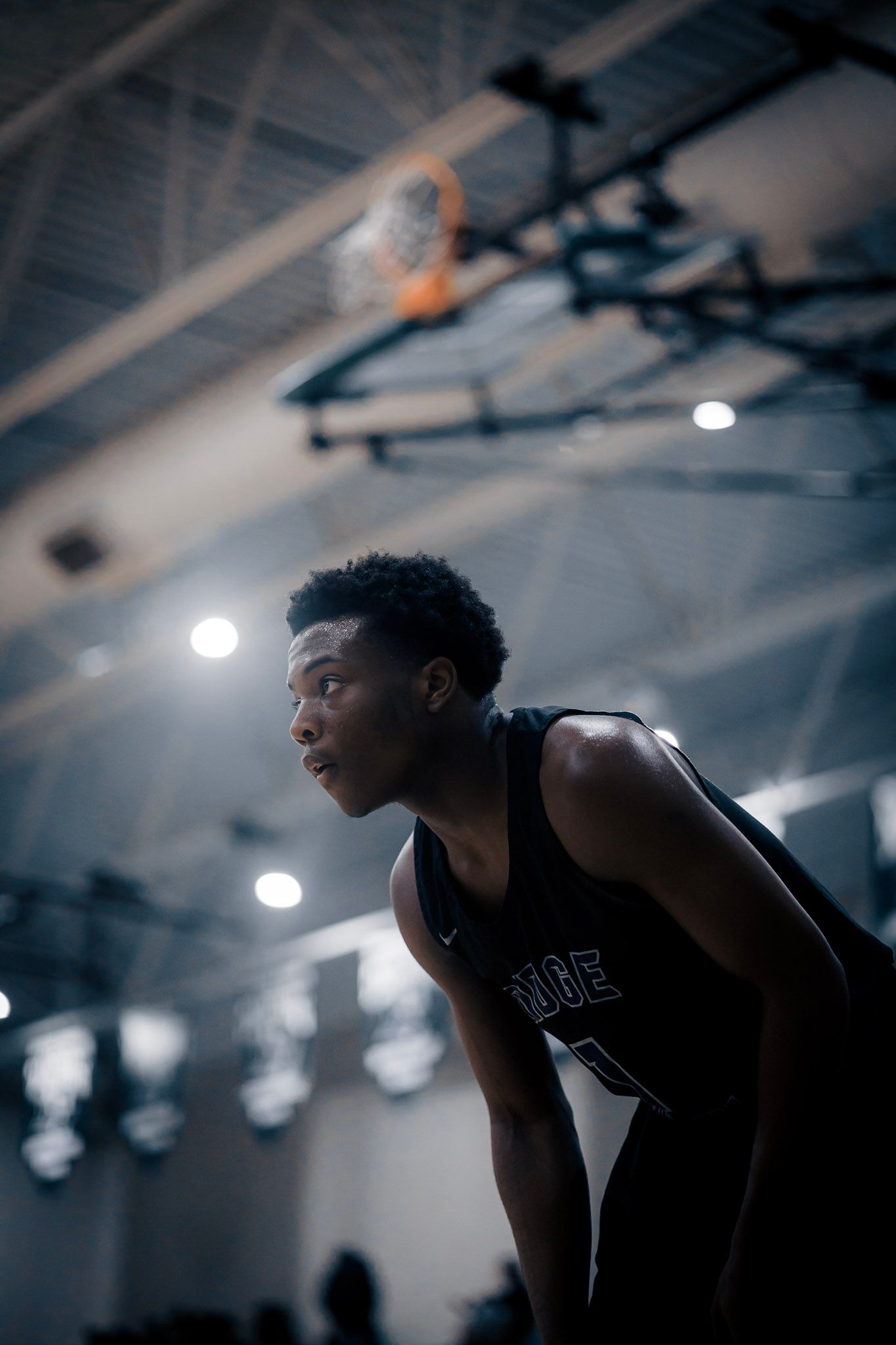Basketball player in black jersey focused during indoor game with stadium lights visible above.