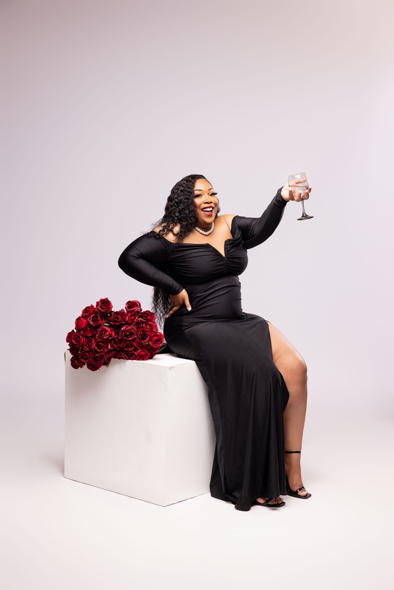 Photo shoot with black dress and red roses on white backdrop.