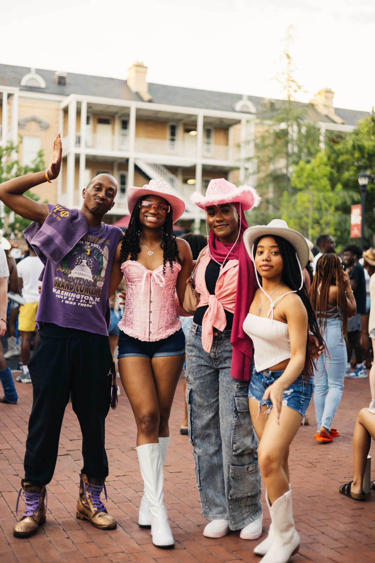 Line dancing performers wearing western boots and casual attire show off dance moves on brick pavement during event.