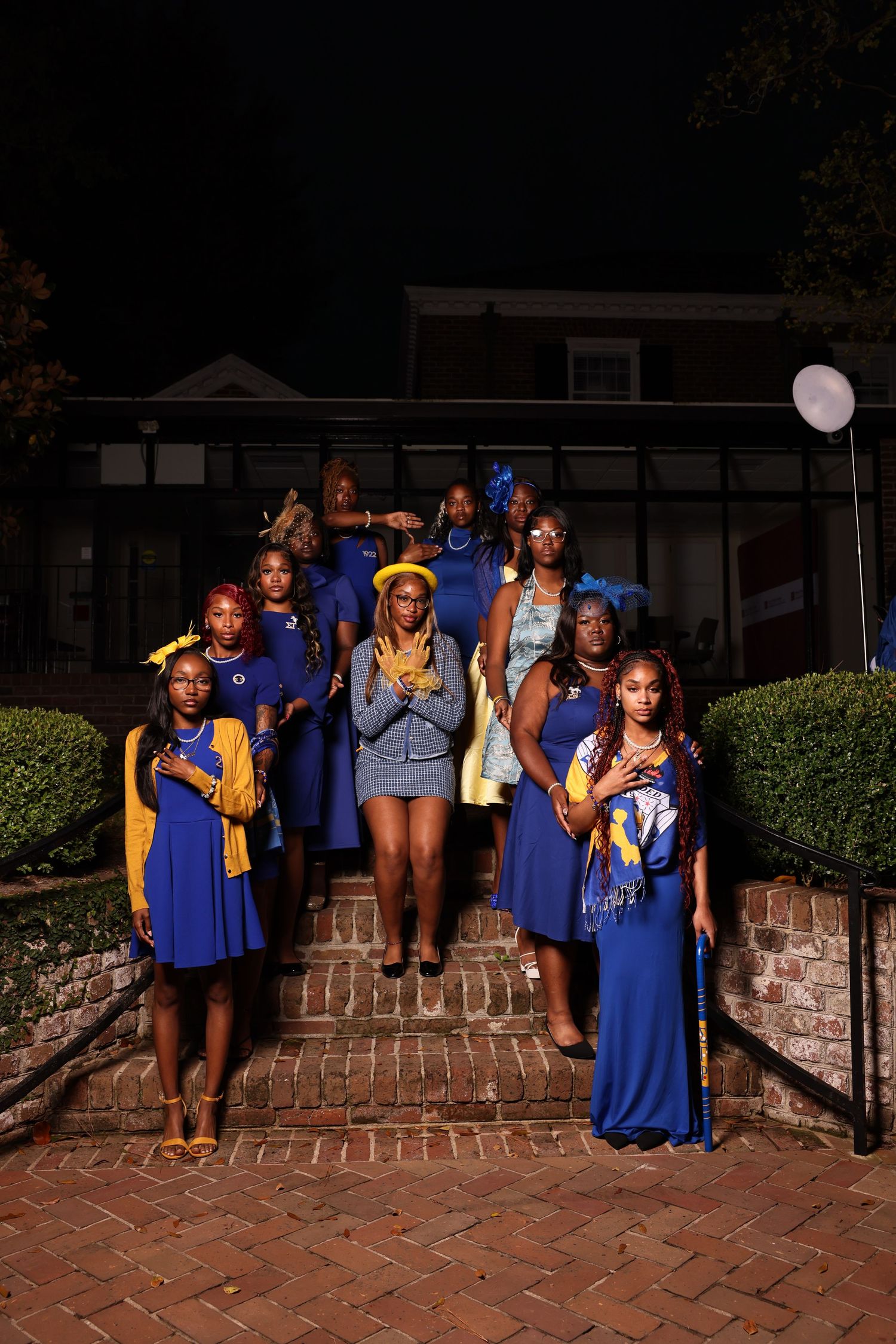 A group in blue dresses and yellow accessories poses on brick steps at night.