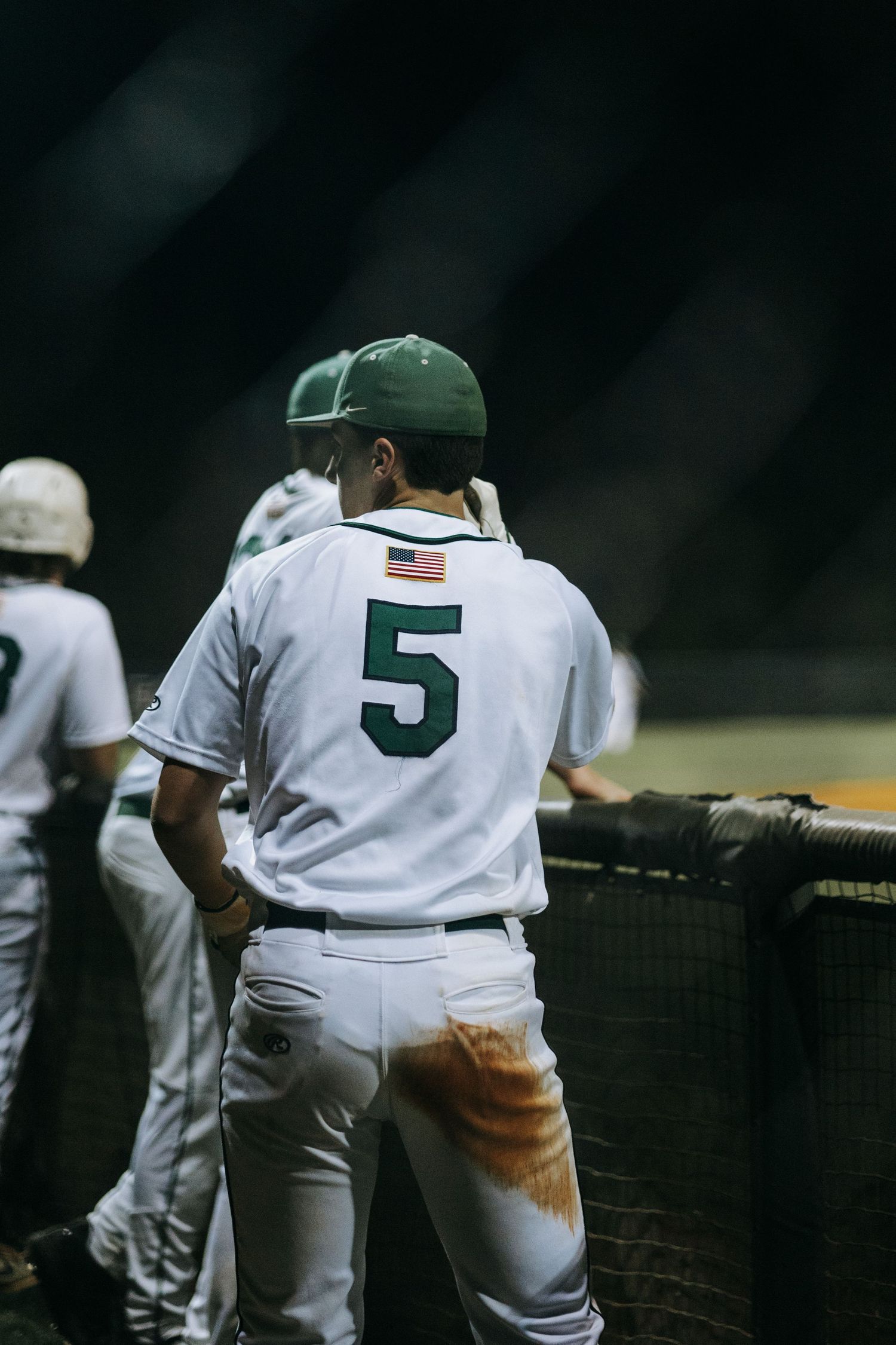 Baseball player wearing jersey number 5 stands at the dugout rail during a game.