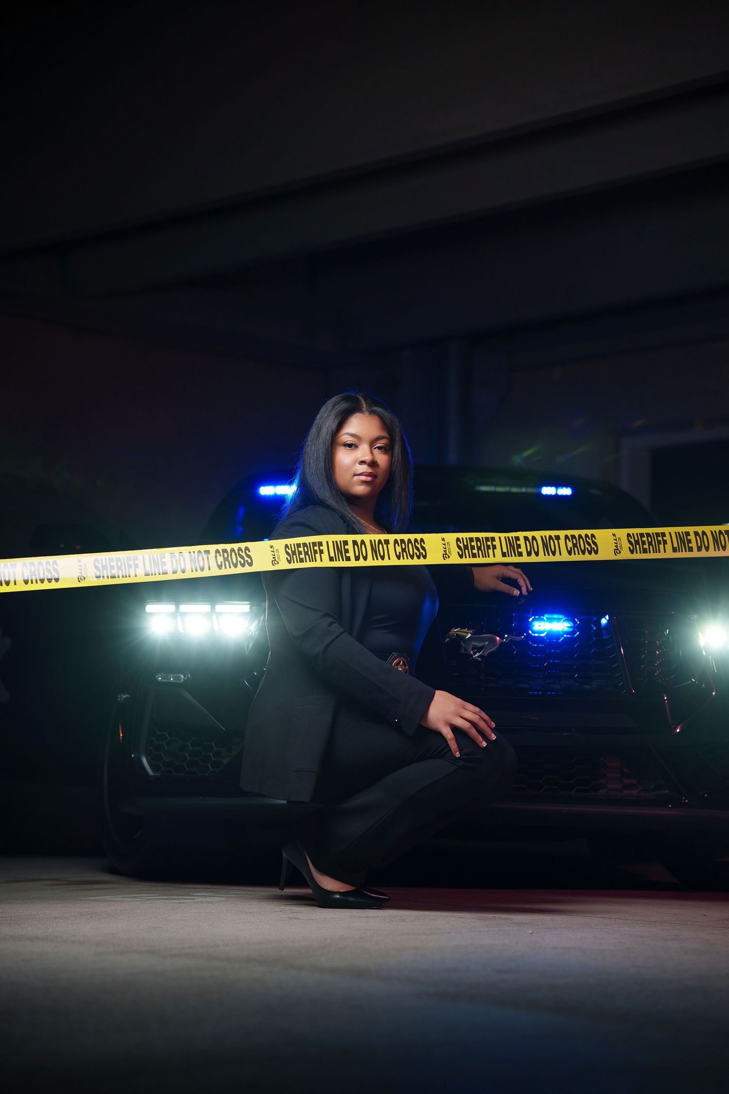 Police crime scene tape cordons off a dark area at night with emergency vehicle lights glowing in the background.