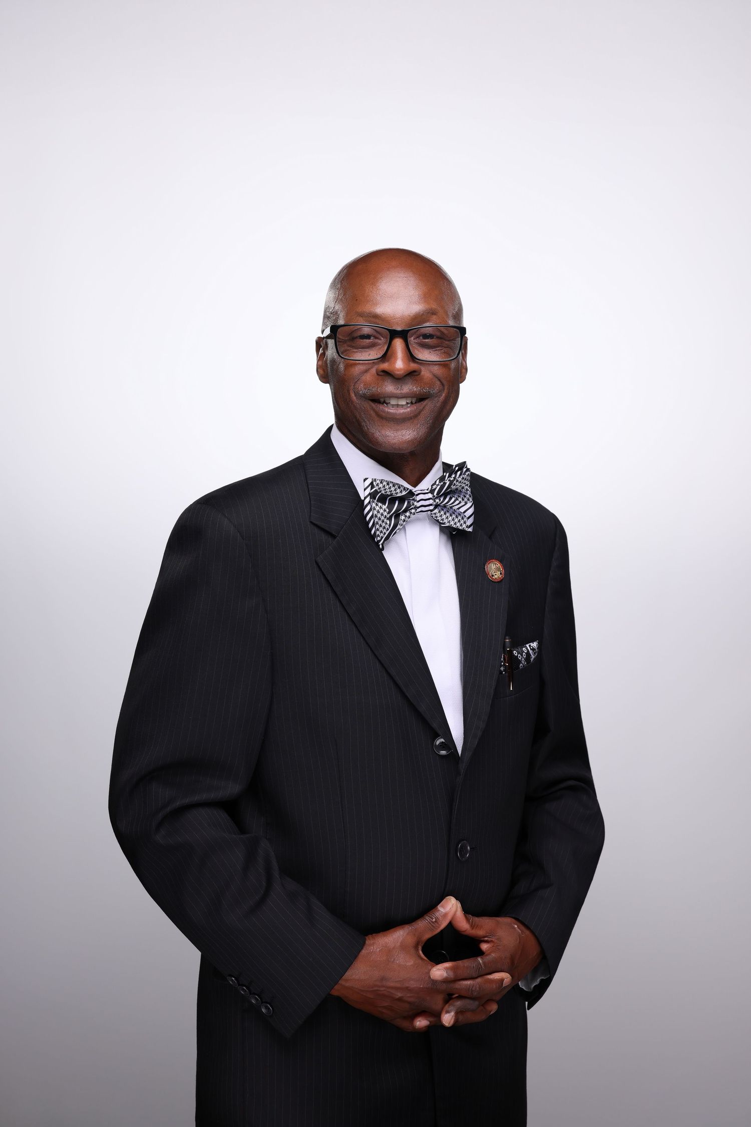 Professional man in black pinstripe suit and patterned bow tie, smiling confidently against a light gray background.