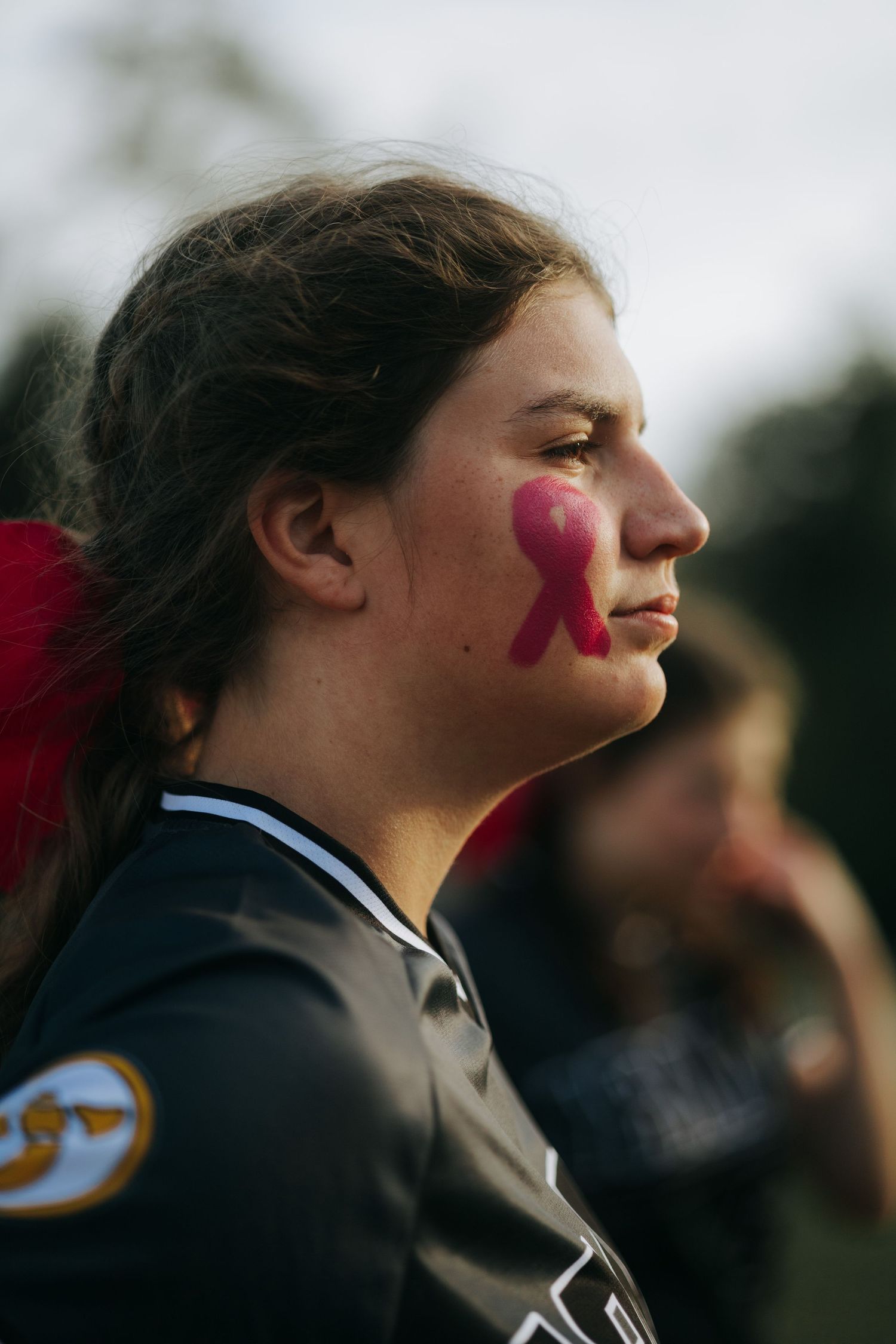 Irmo HS Player with pink ribbon face paint watches game from sideline.