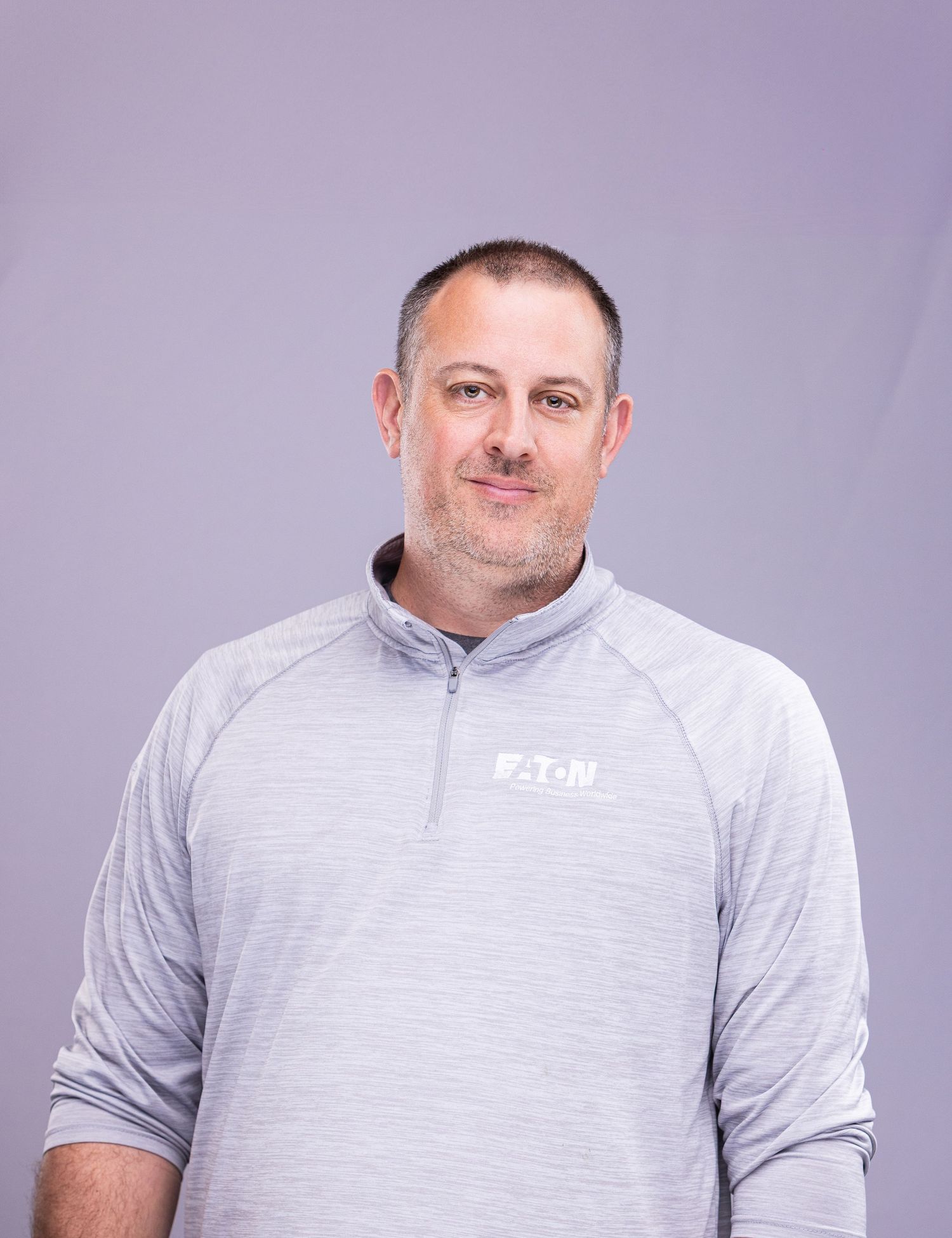 Professional portrait of person in gray quarter-zip pullover with Eaton logo against purple background.