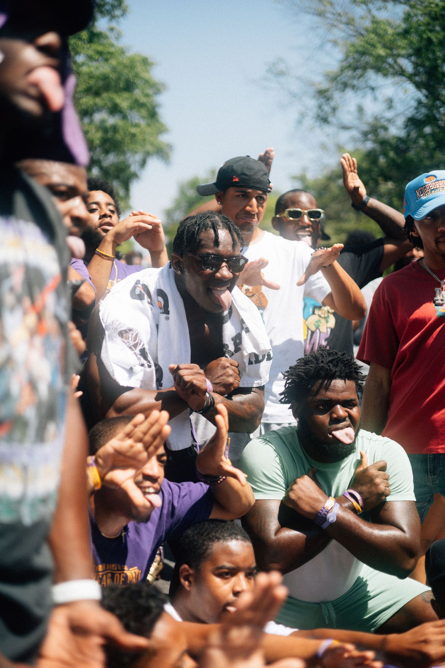 An enthusiastic crowd cheers and reacts emotionally outdoors on a sunny day with trees visible in the background. USC Hip Hop Wednesday
