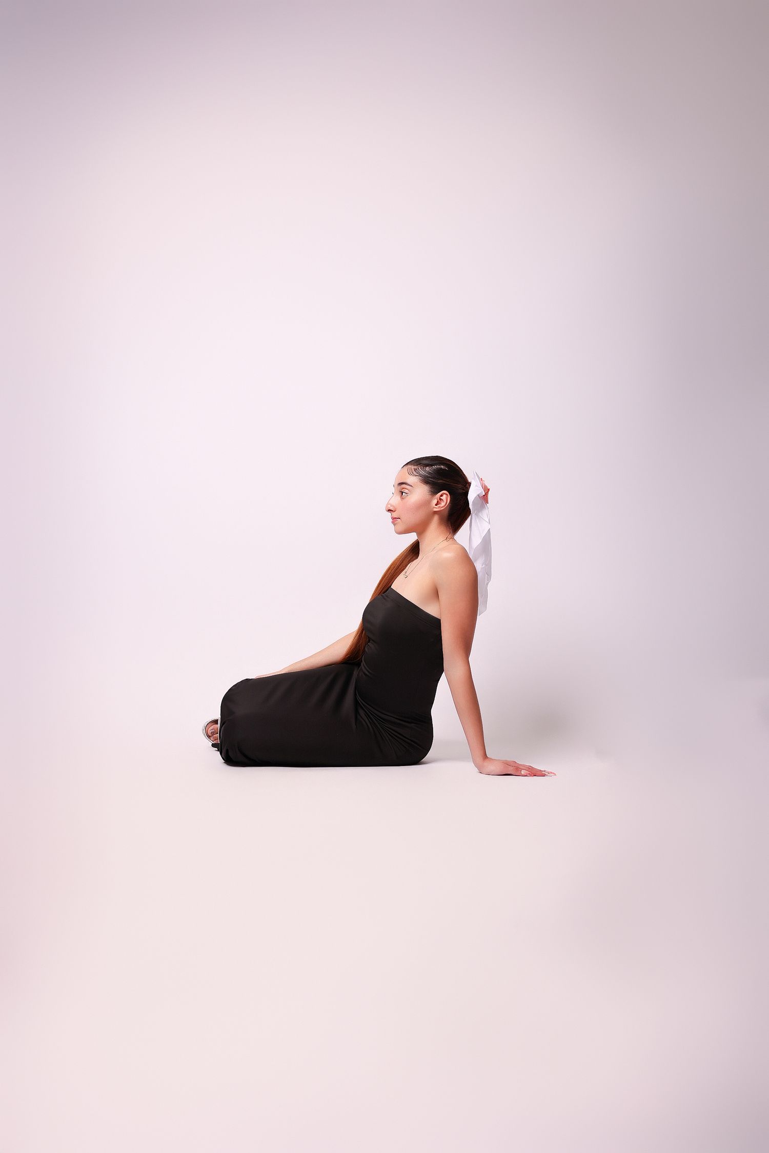 A figure in a black leotard performs a graceful dance pose on a white studio backdrop.