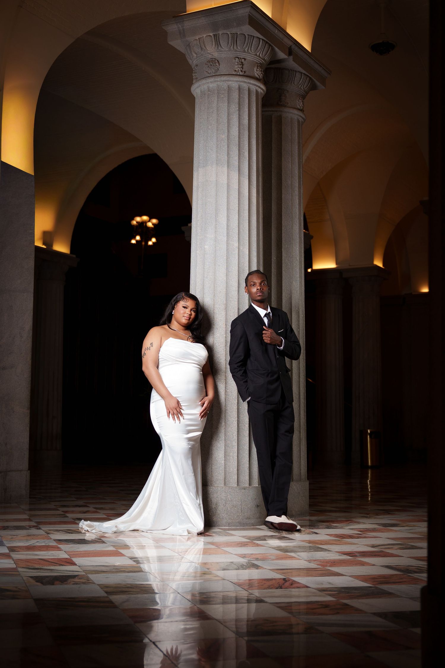 A romantic wedding couple poses in a dramatic series of shots against stone columns in a dimly lit corridor.