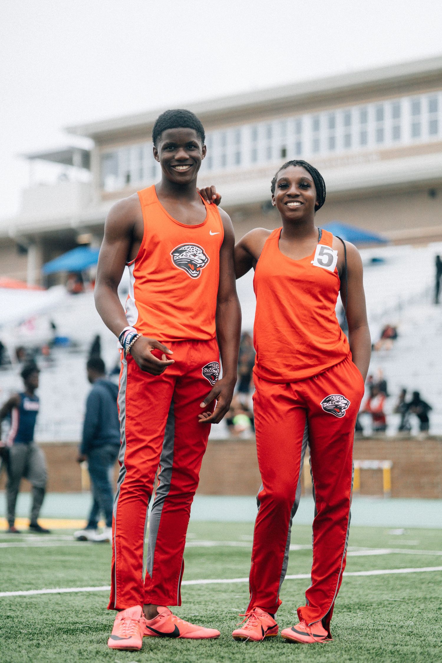 Track athletes in bright orange uniforms smile together on field during meet.