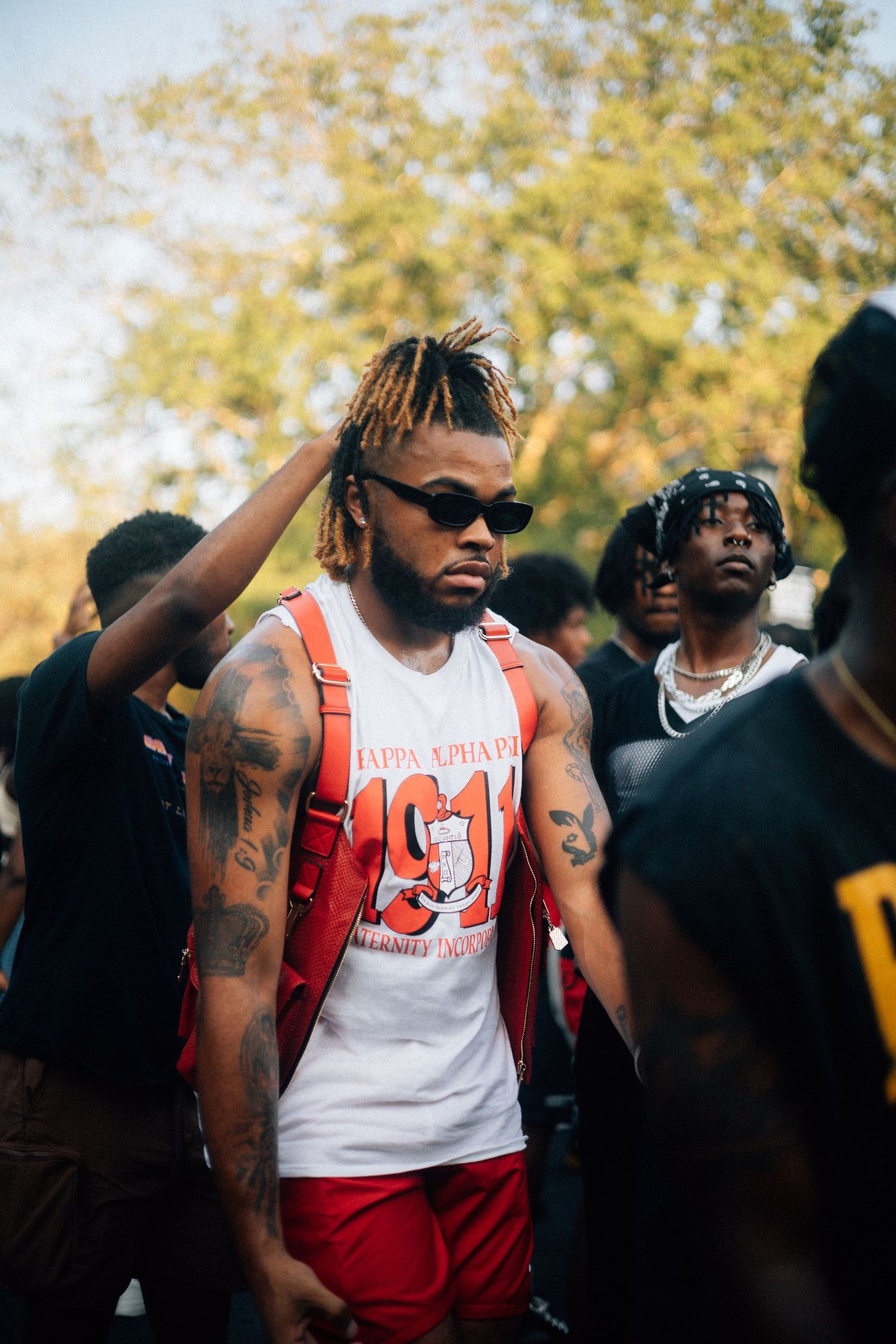 Person wearing a white tank top and red shorts with sunglasses stands amongst others outdoors on a sunny day.USC Hip Hop Wednesday