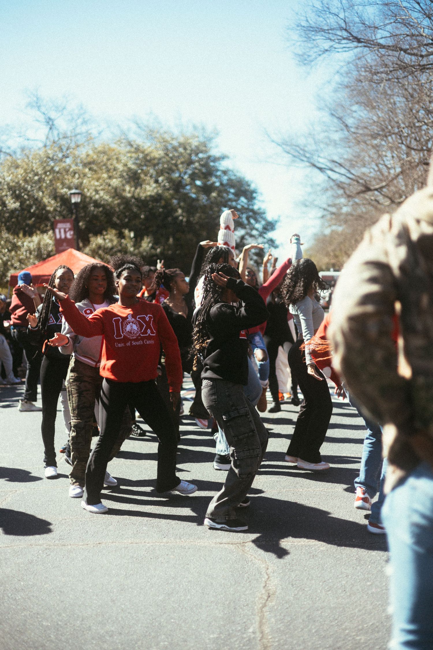 A crowd of people dancing and celebrating outdoors on a sunny day with trees in the background. USC Hip Hop Wednesday