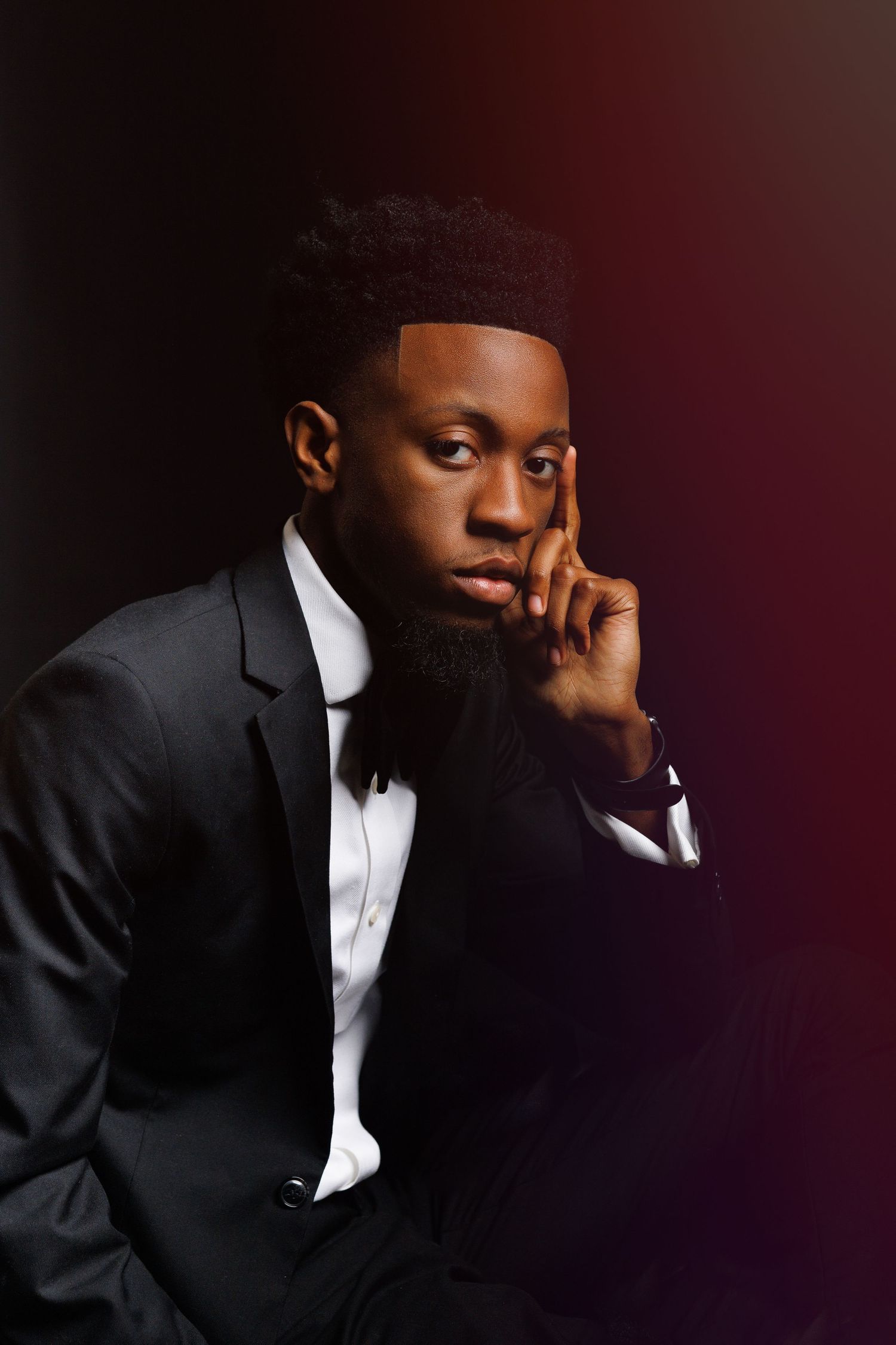Portrait of a contemplative man in formal black tuxedo and bow tie against dark background with dramatic lighting.