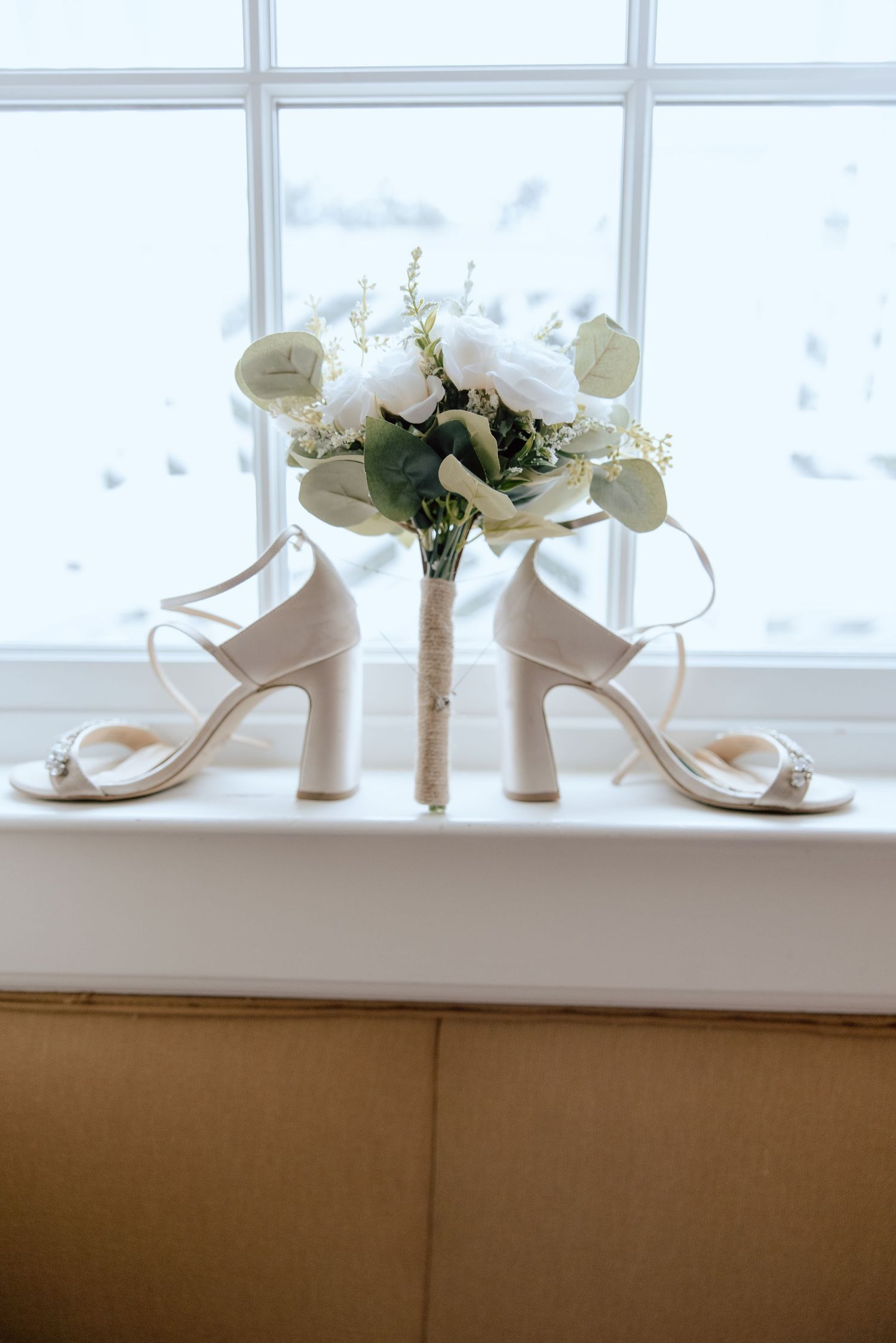 White bridal shoes and floral bouquet displayed on windowsill.