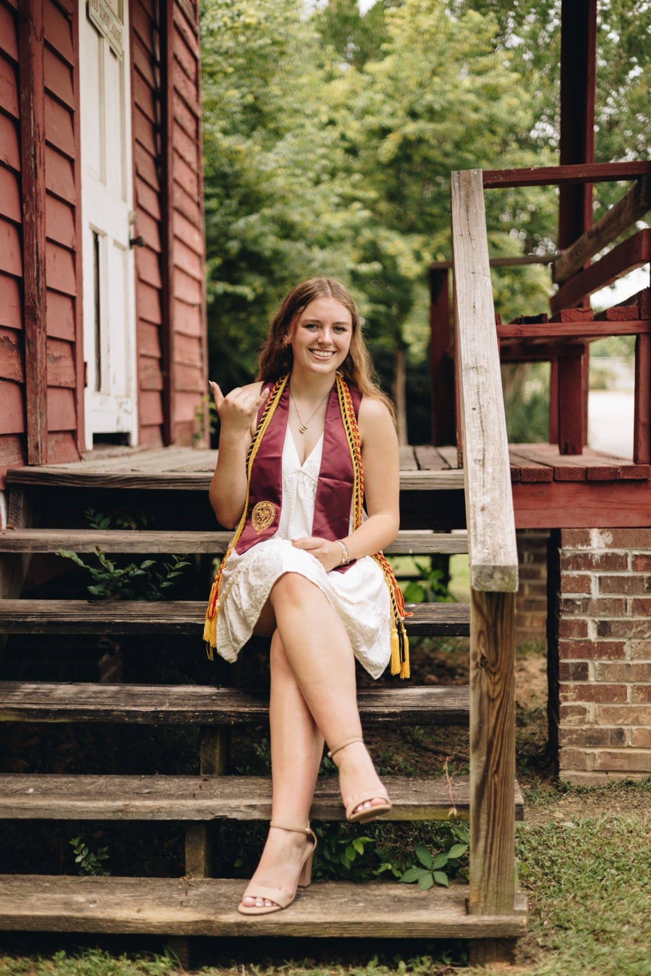 Young woman in summer dress sits on rustic wooden steps of red house.