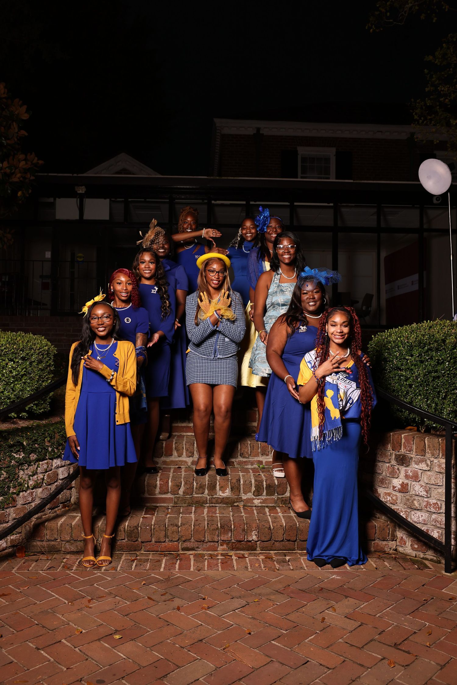 A group in blue graduation gowns poses together on brick steps at night during a celebratory photoshoot.