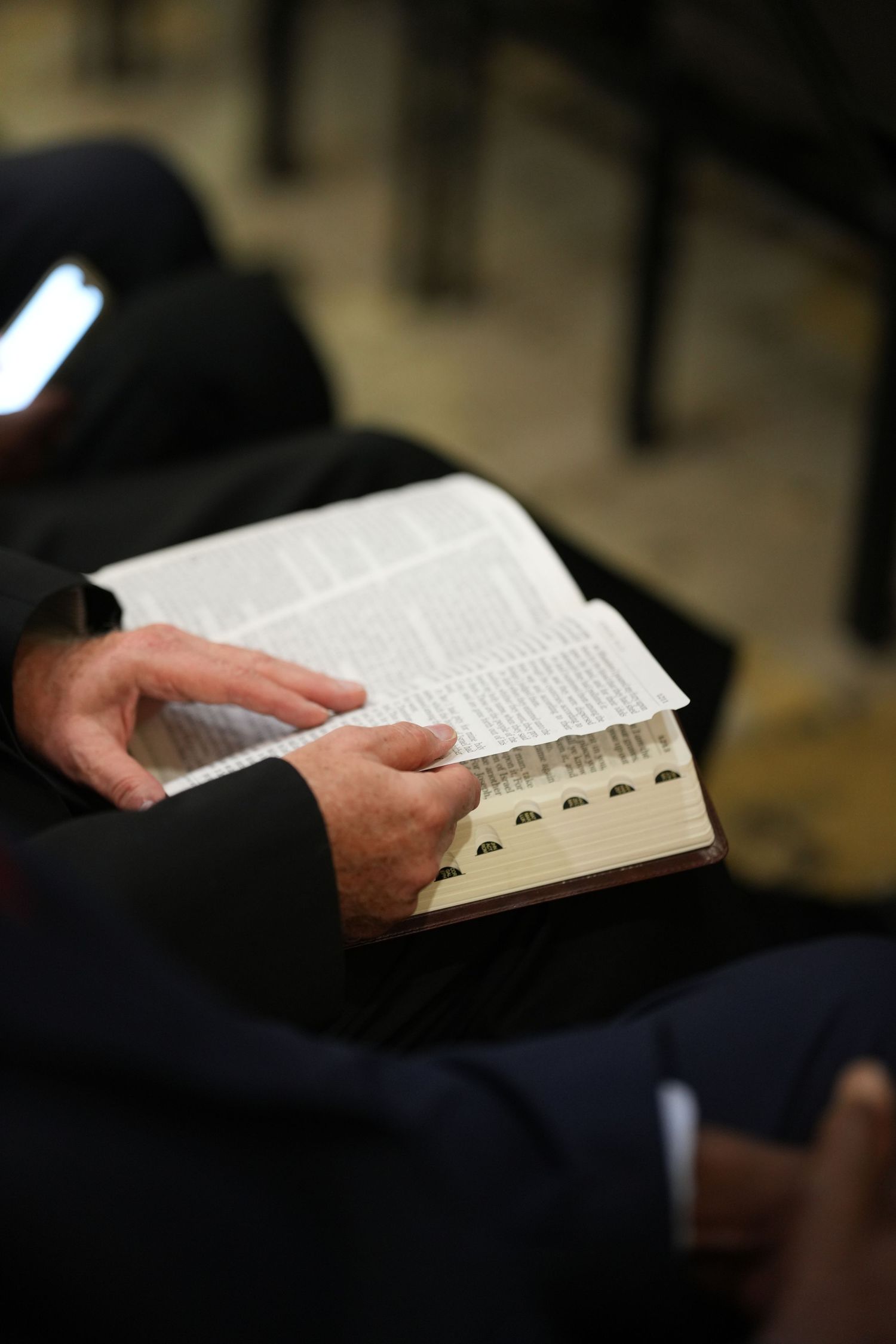 Man in suit reading open Bible, holding pages with both hands during church service.