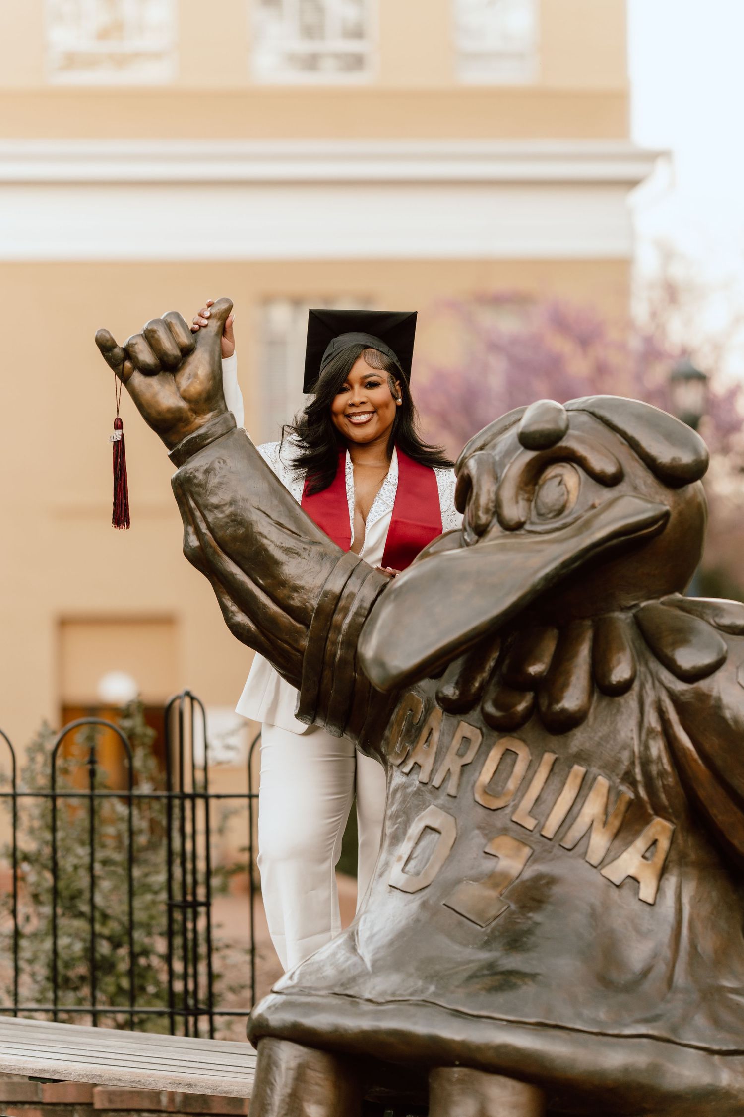 Graduate poses with UofSC University's iconic limestone sculpture during commencement celebration.