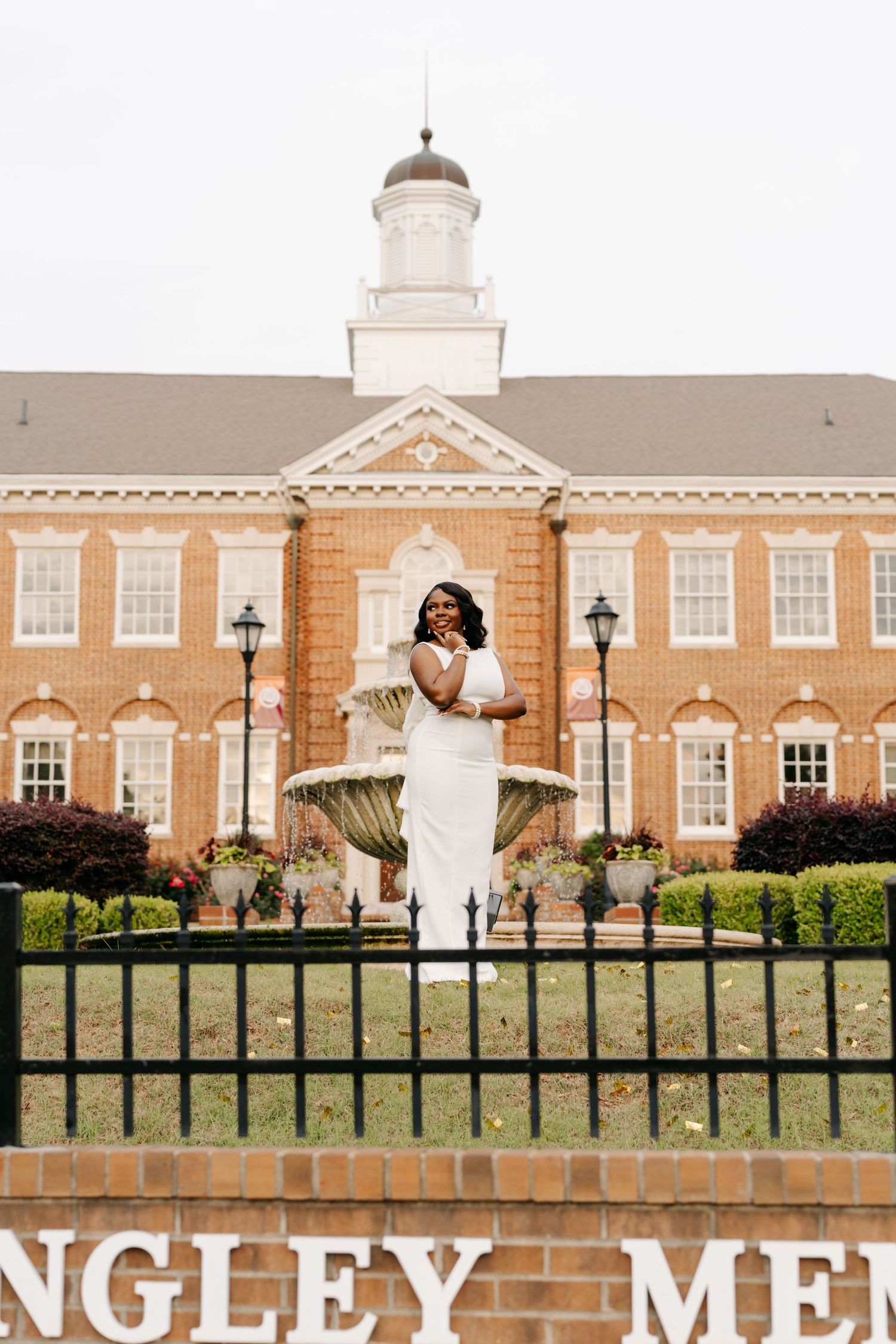 Woman in white dress posing by fountain in front of historic brick building with cupola at Langley Memorial.