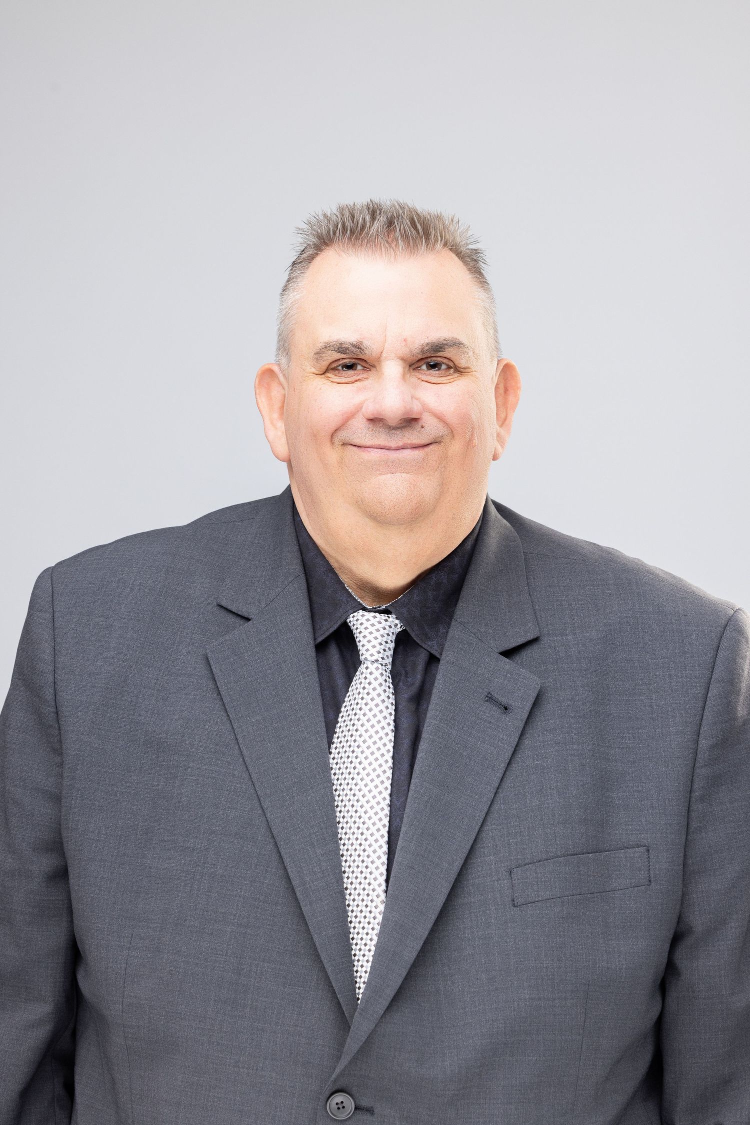 Professional headshot series of a person in a dark gray suit and polka dot tie against a light background.