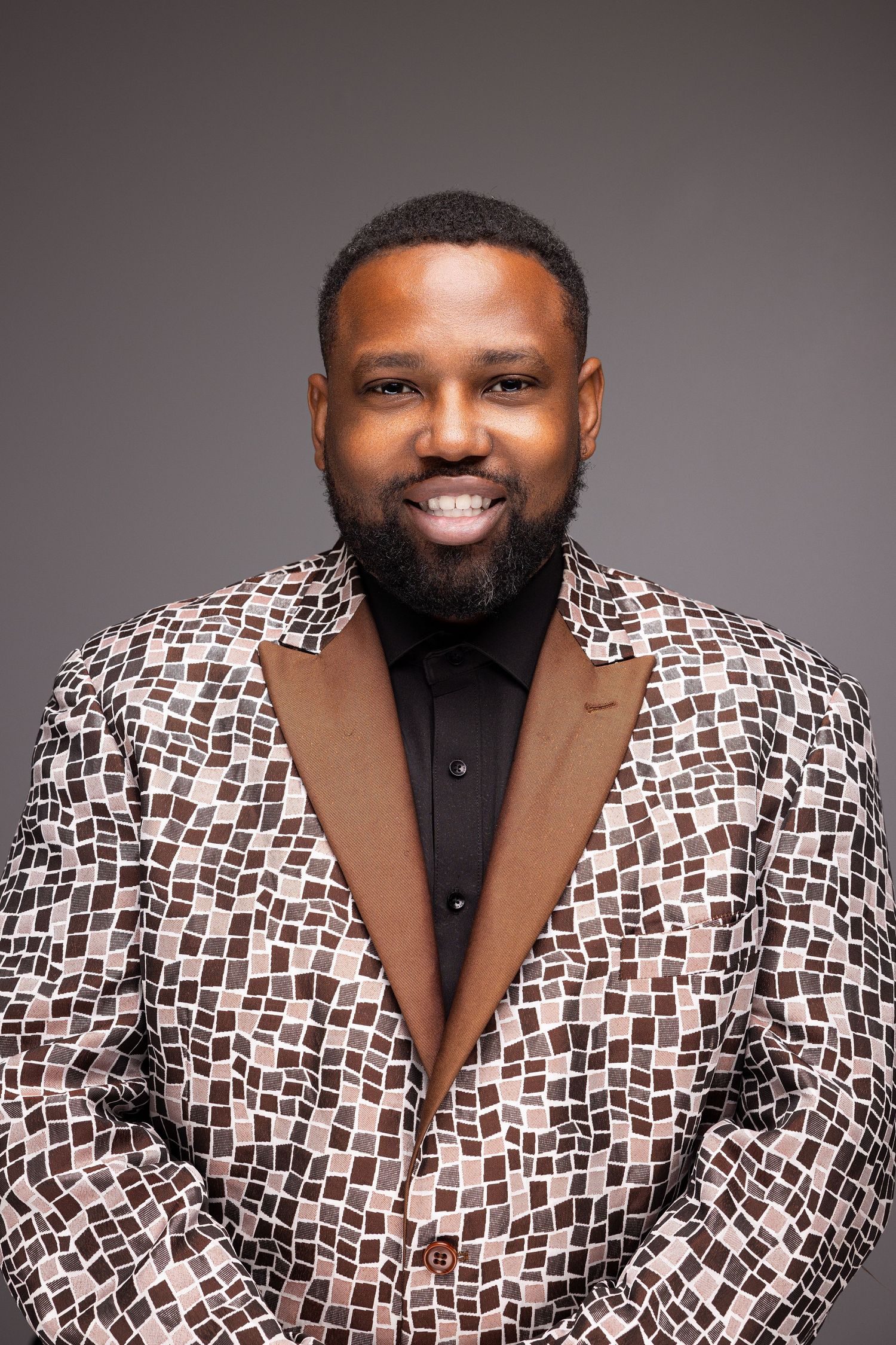 Professional studio portrait showing a person wearing a stylish black and white patterned blazer with a black shirt.
