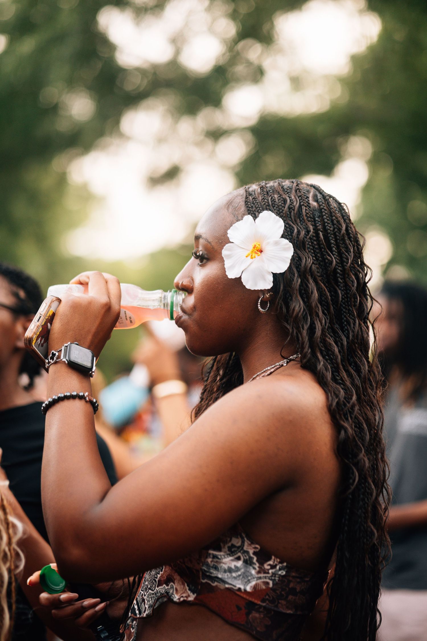 A series of artistic portraits showing a person wearing a white flower while drinking from a bottle against a bokeh background.