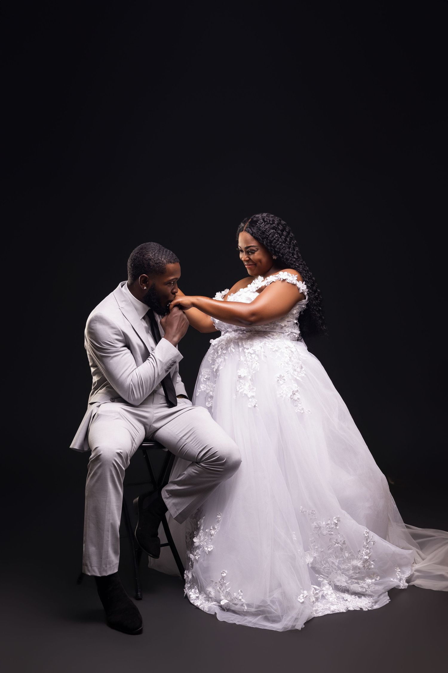 Romantic moment between couple in white formal wear against dark background.