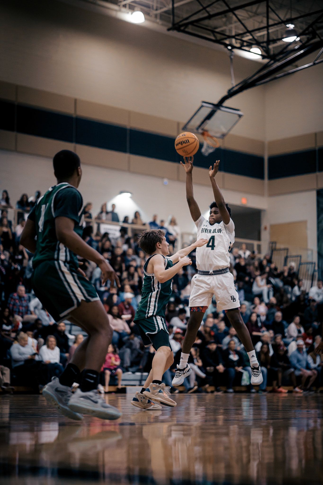 Basketball player takes jump shot while defenders try to block during competitive game.