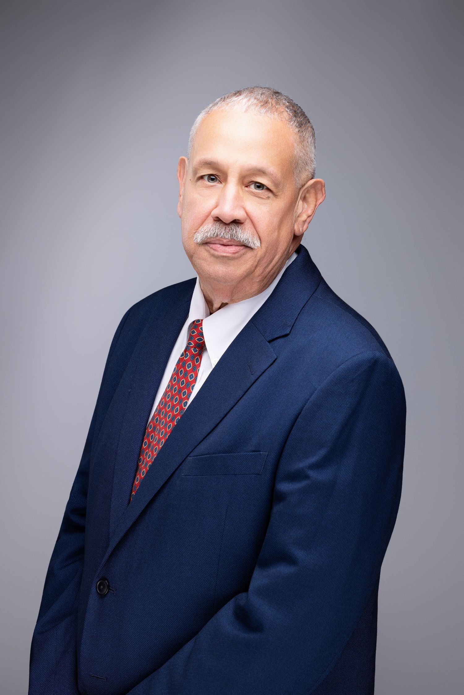 Professional headshot series showing different angles of a person in a navy suit and red tie against a gray backdrop.