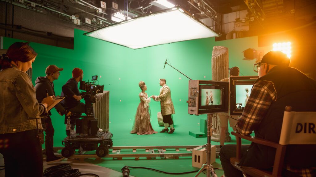 Film crew working on a green screen stage with lighting equipment and camera setups during a video production shoot.