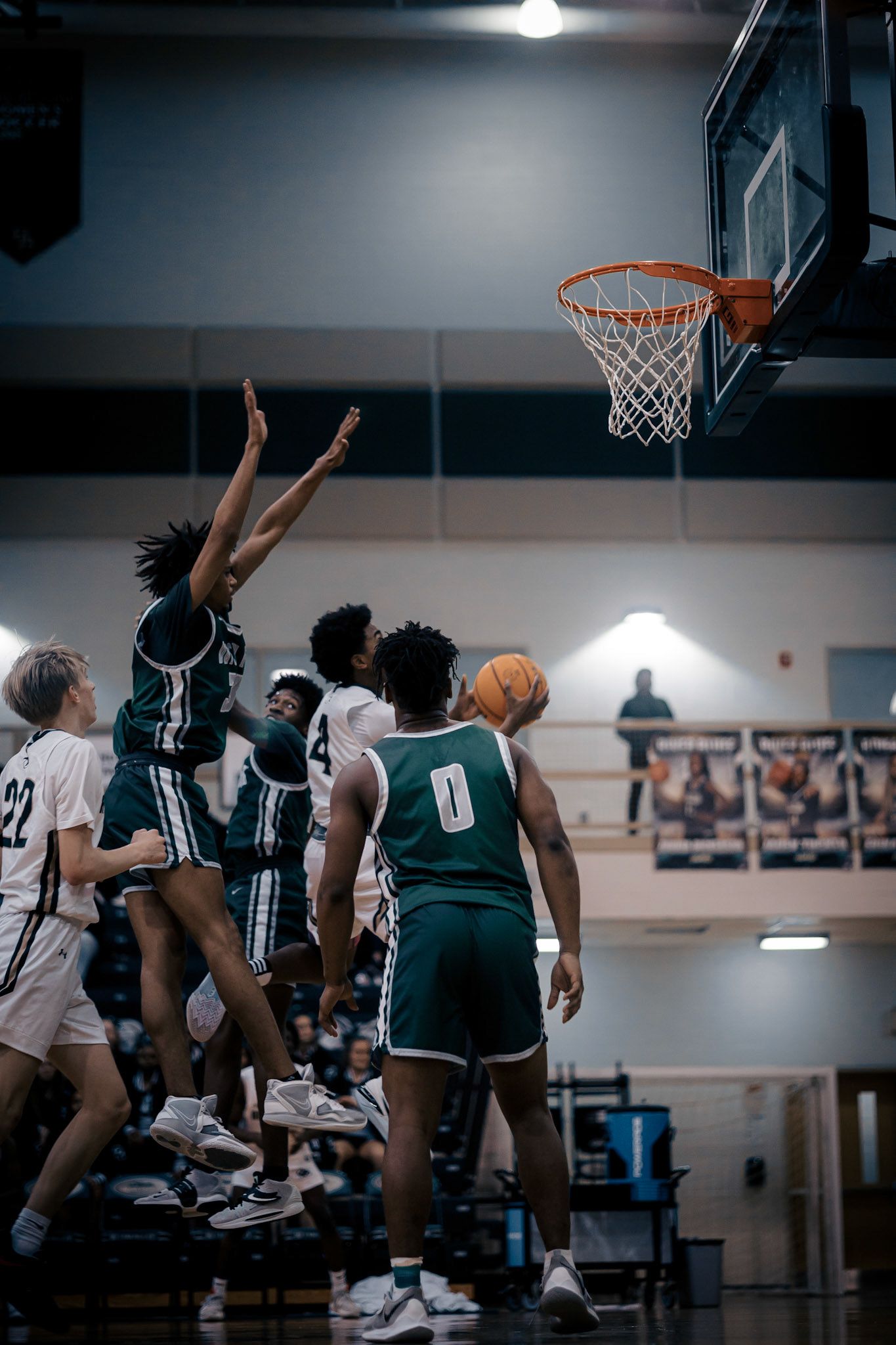 Basketball players leap high for the ball during an intense game under indoor gym lighting.
