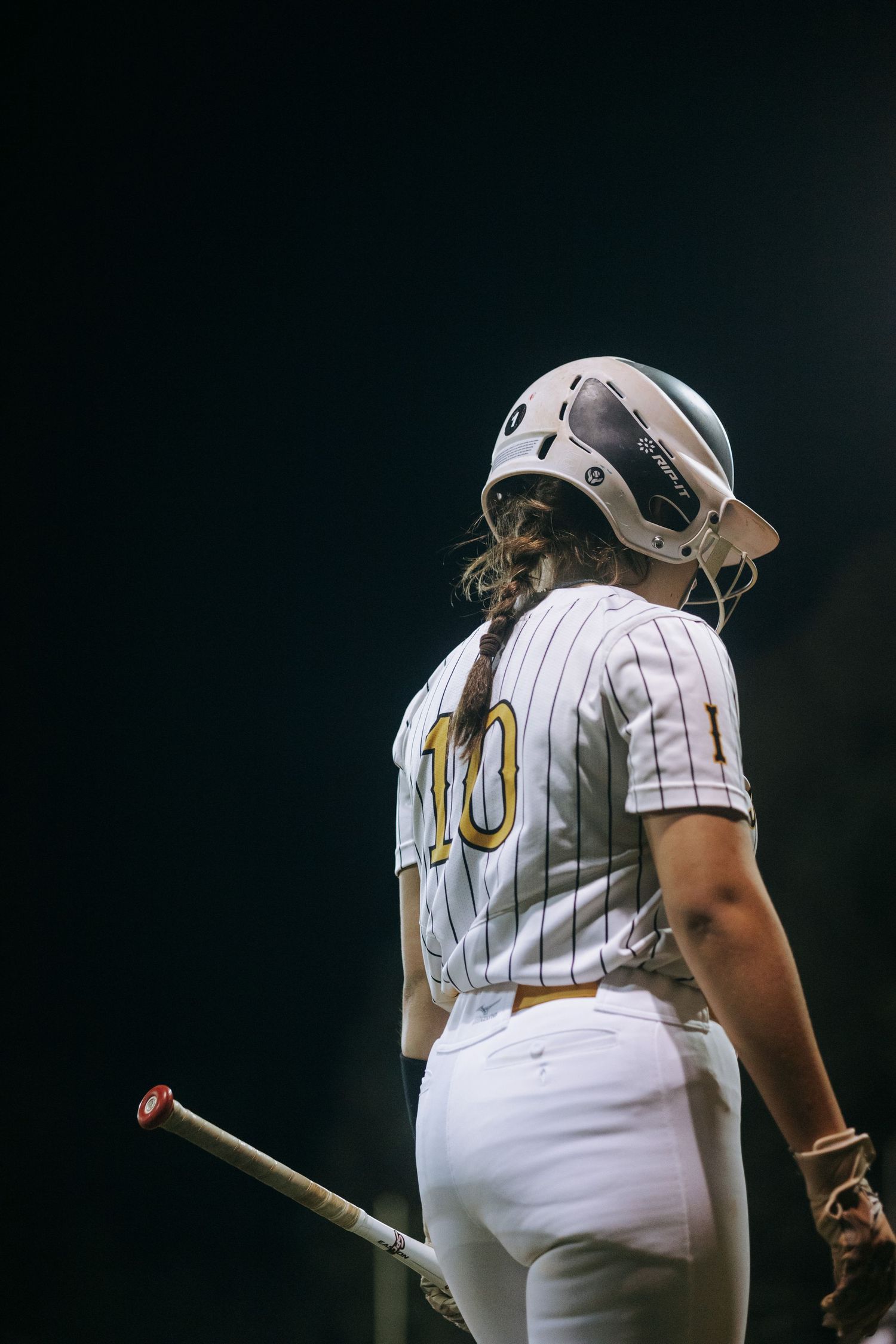 Softball player wearing jersey number 10 holds bat during game.