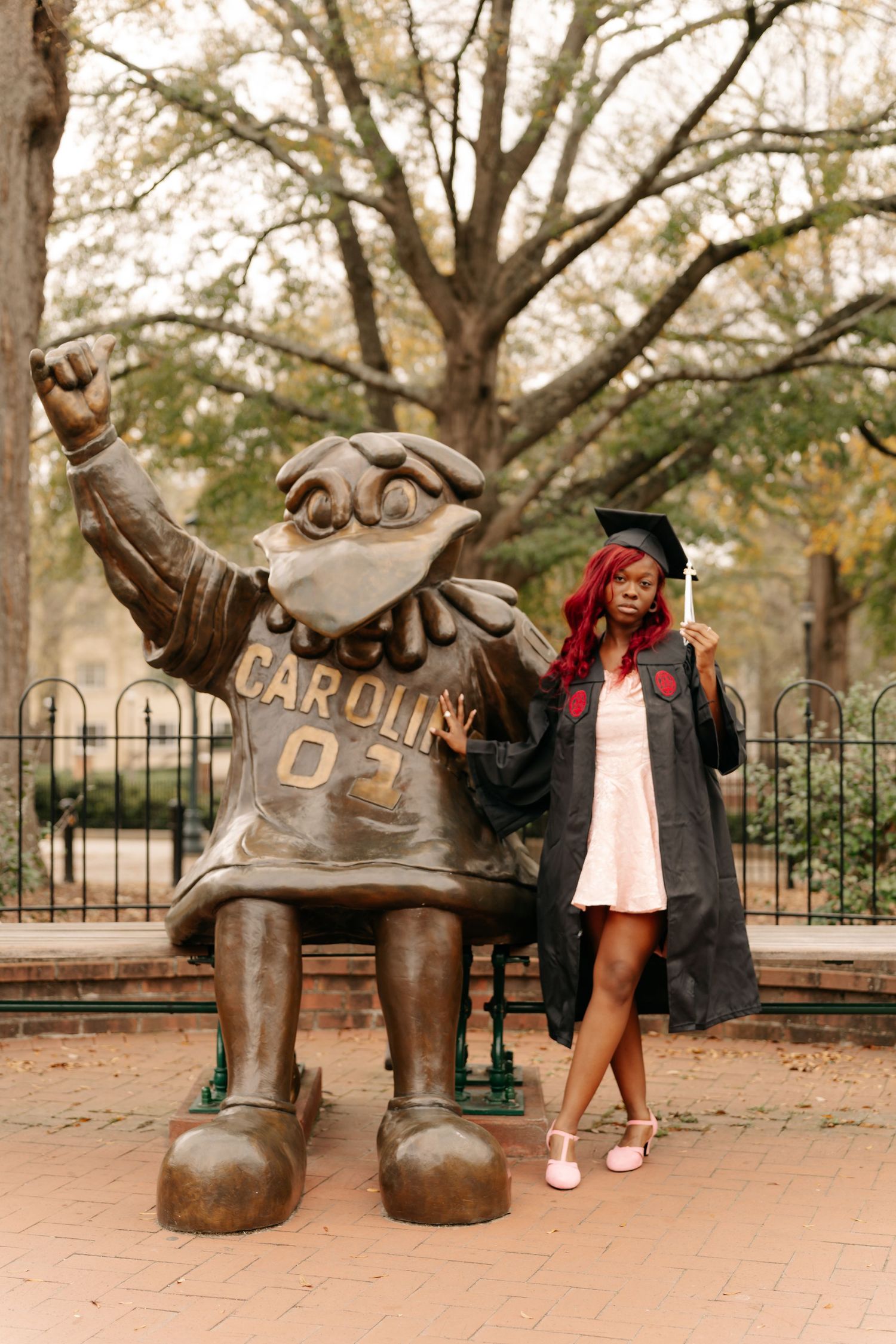 A series of four photos showing someone posing playfully with a bronze sculpture in a park-like setting at the University of South Carolina.