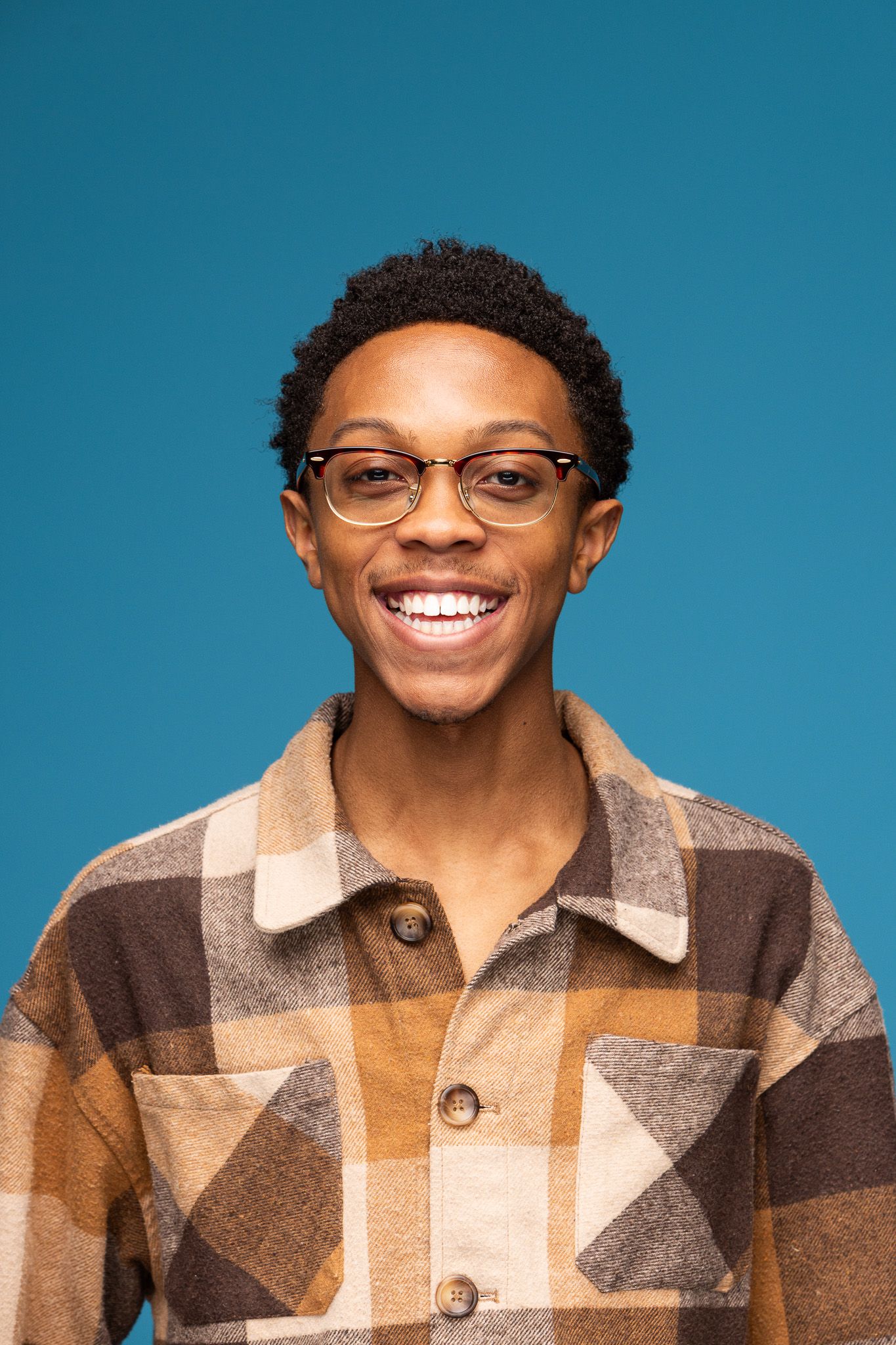 Professional portrait of person in plaid flannel shirt and glasses against blue background.