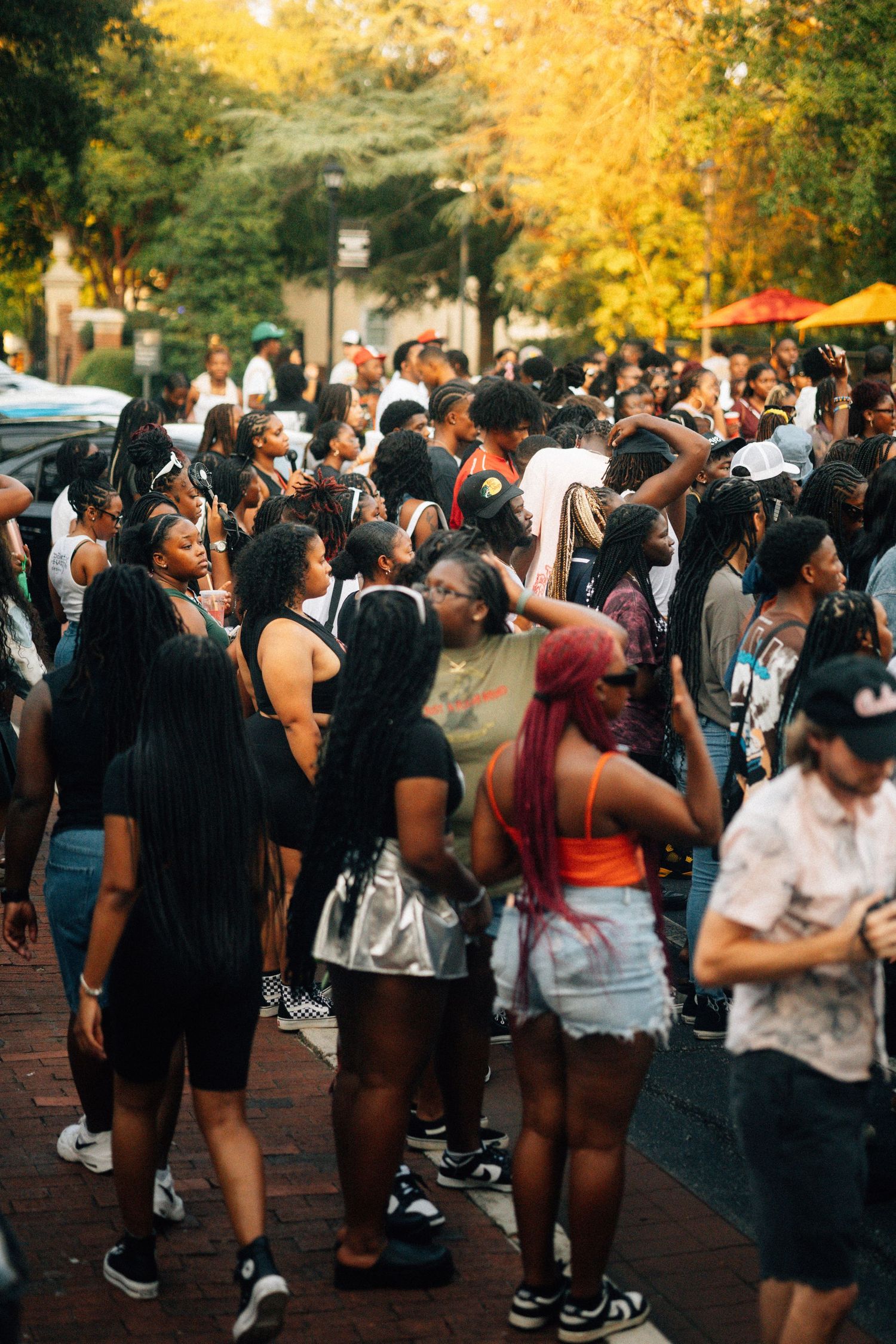 A large crowd of people gathered at an outdoor event during golden hour with autumn trees in the background. USC Hip Hop Wednesday