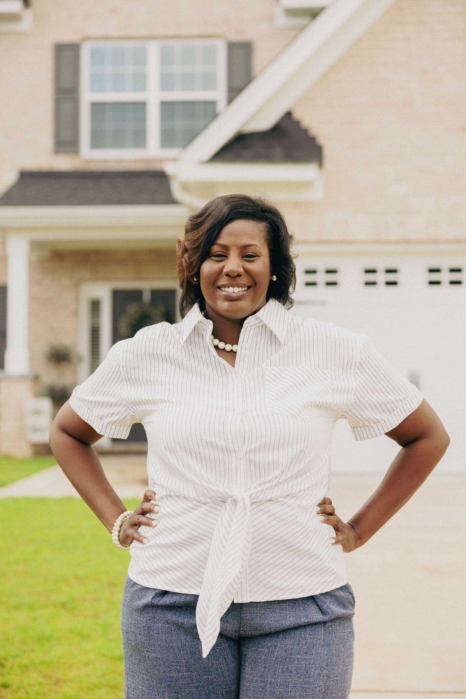 Casual outdoor portrait against white house wearing striped button-down shirt.