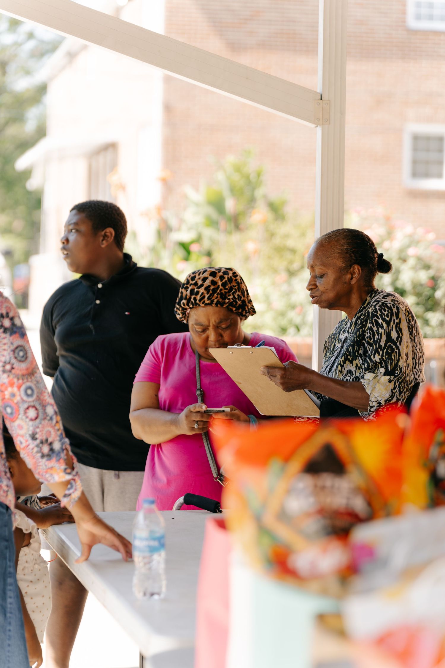 Three people reviewing documents at an outdoor community event table with colorful decorations in the foreground.