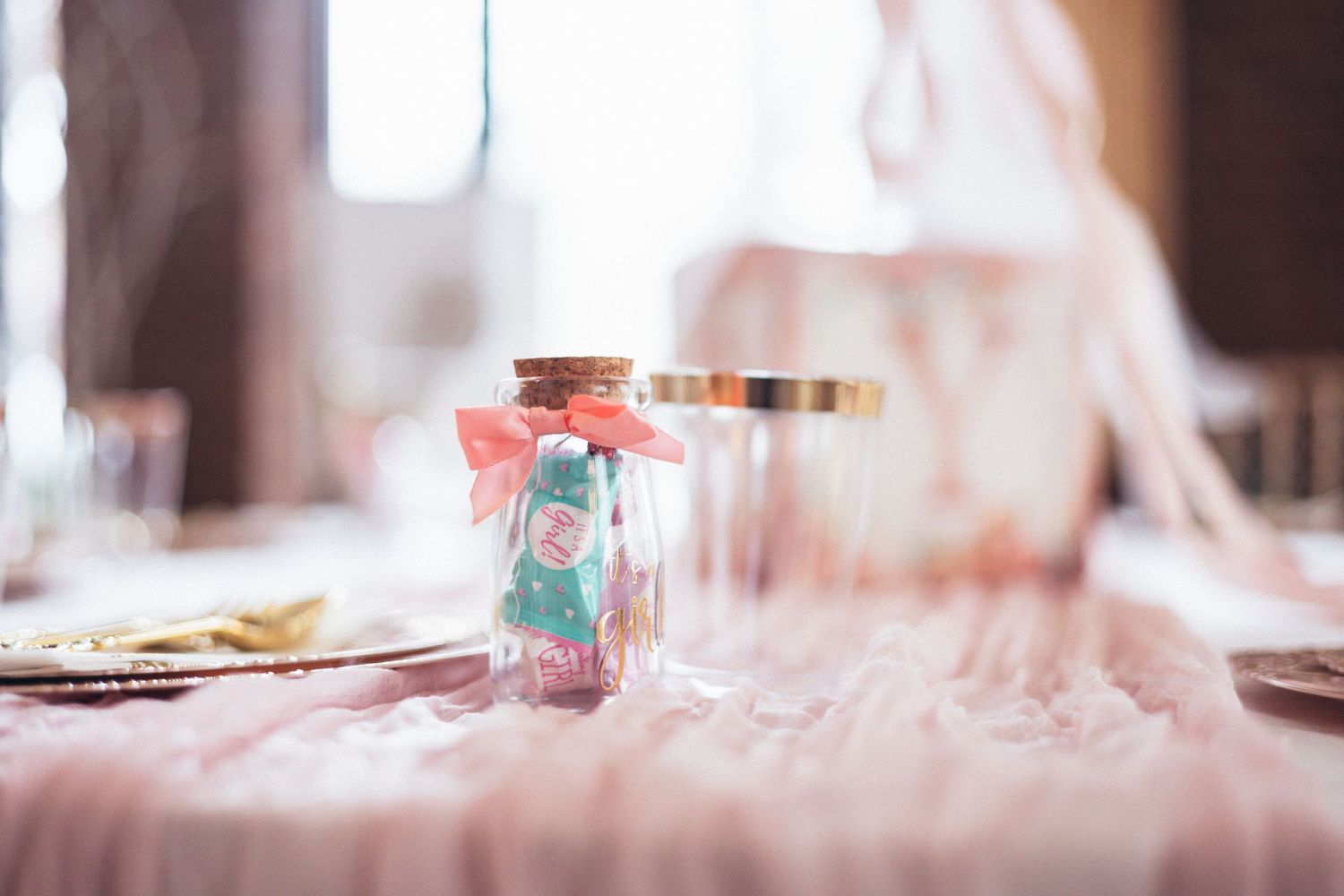 Small glass bottle with cork stopper filled with colorful candies and pink bow, displayed on elegant table at wedding reception.