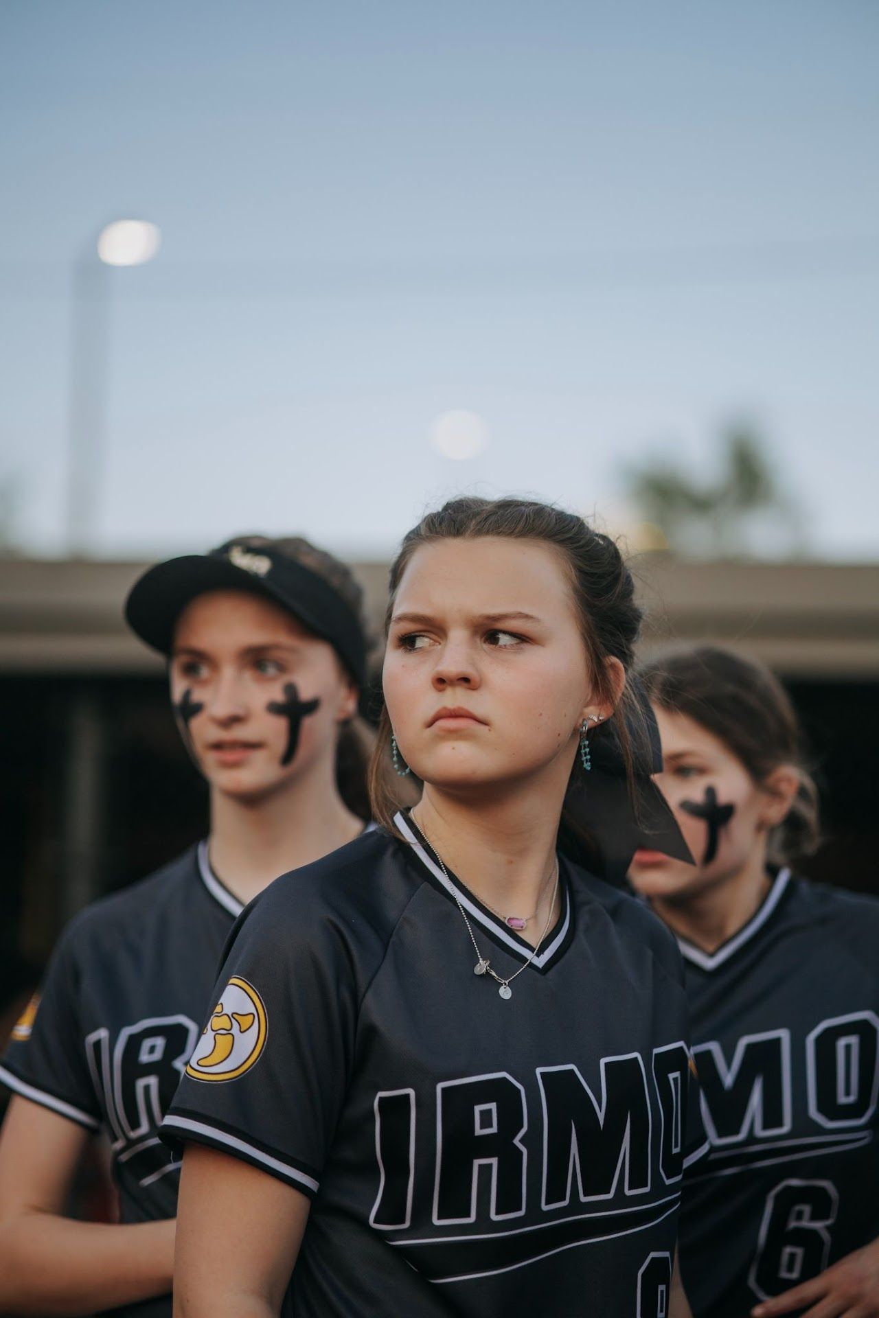 Irmo HS Softball team members in dark uniforms stand together during golden hour.