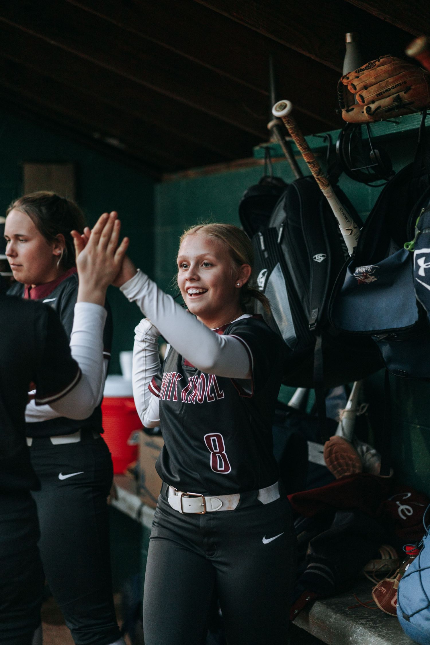 Players celebrate in the dugout during a softball game, showing team spirit and excitement.