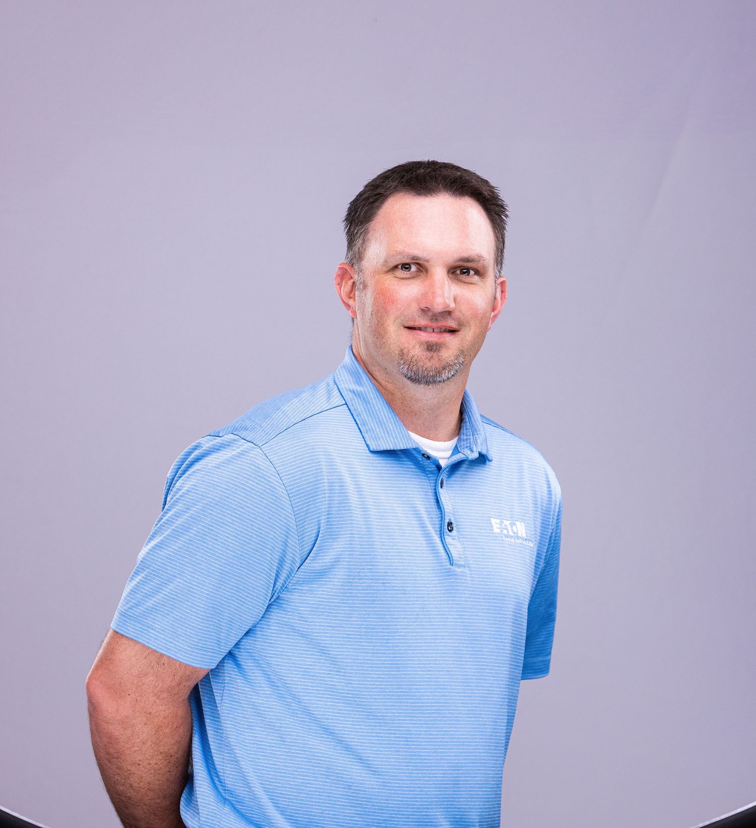 Professional portrait of person wearing light blue polo shirt against purple backdrop.