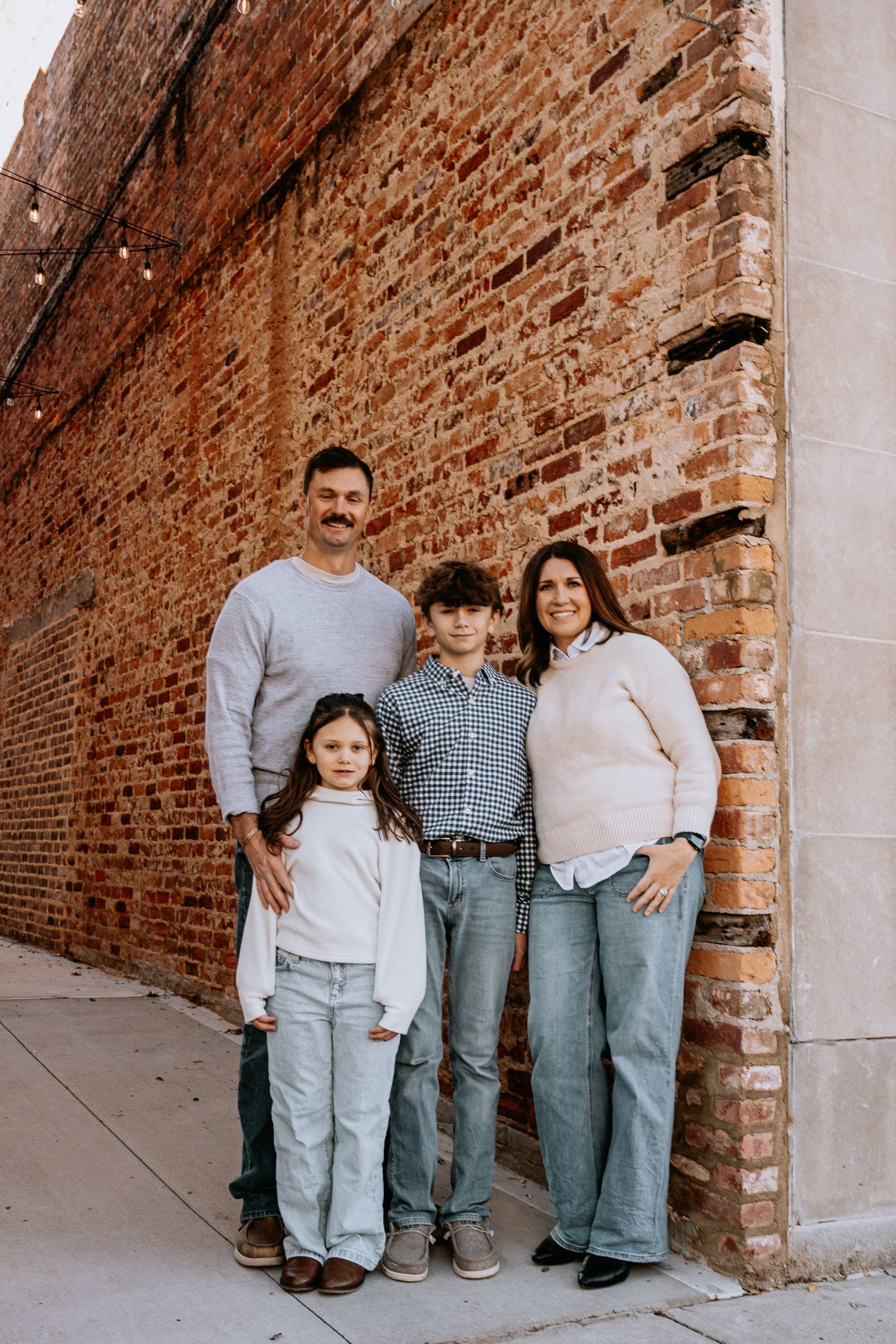 Family of four poses against brick wall during casual portrait session.