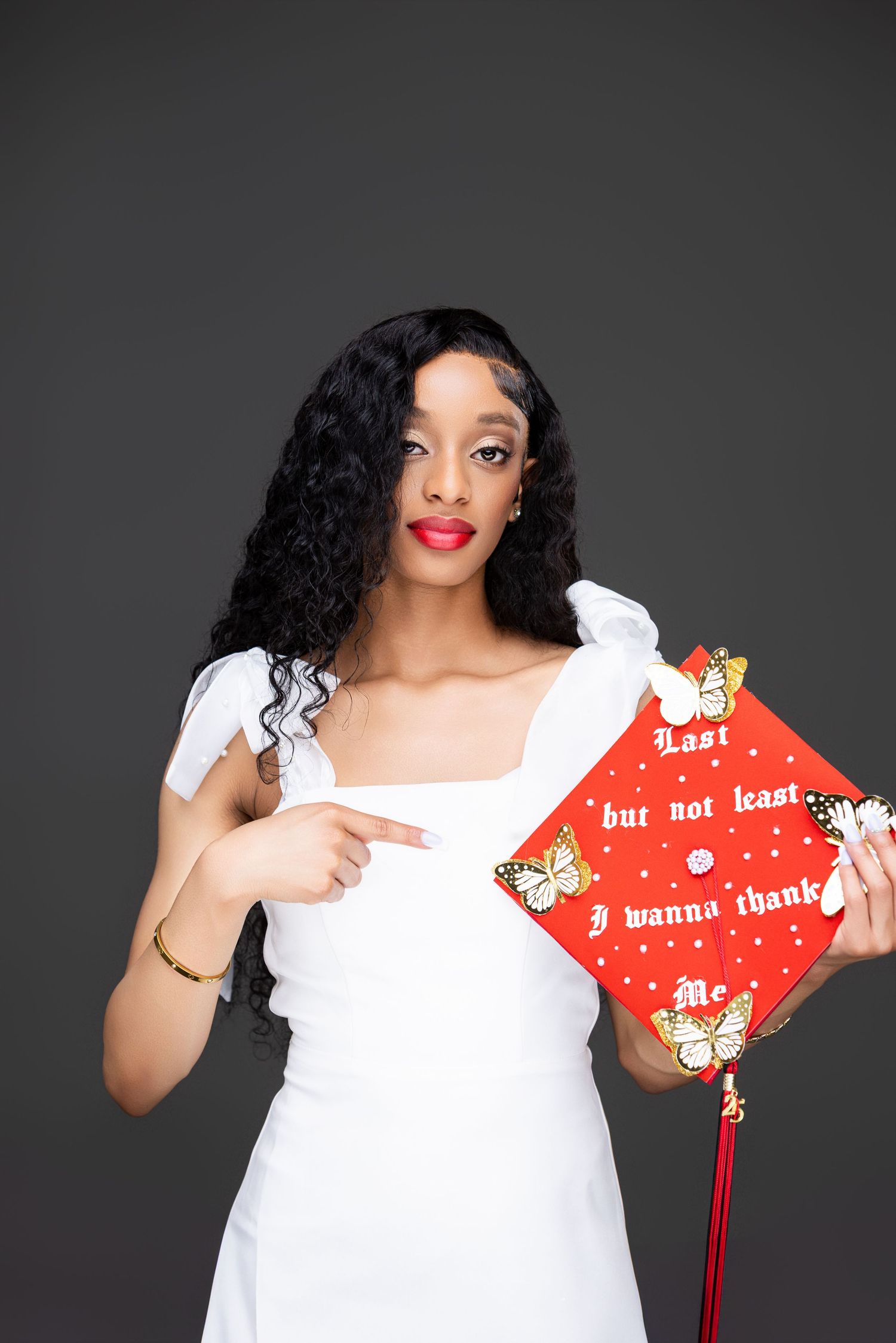 Woman in white dress holding red decorative pillow with text against dark background.
